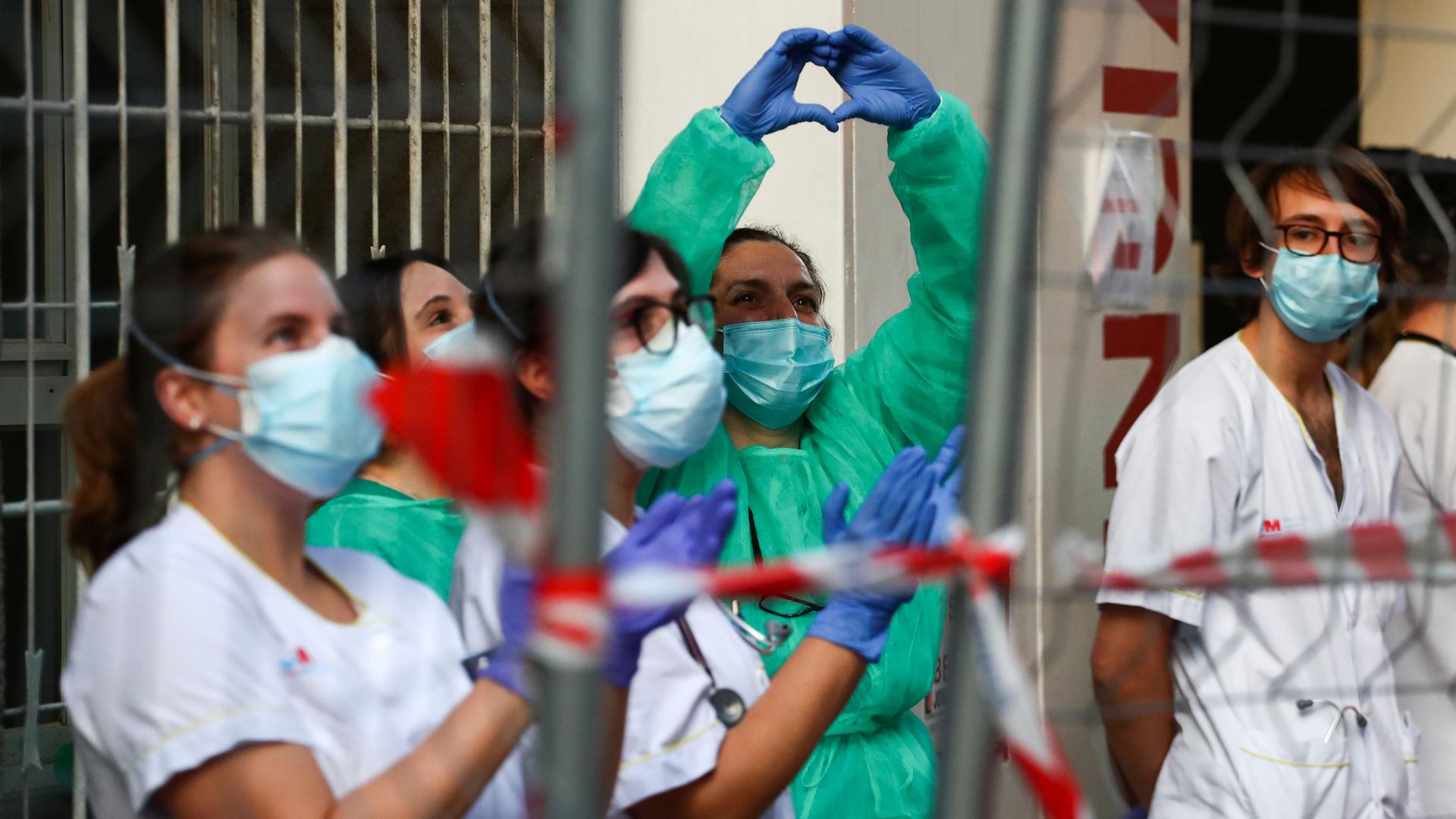 Several health care workers are shown wearing protective suits and one woman making a heart shape with her hands.