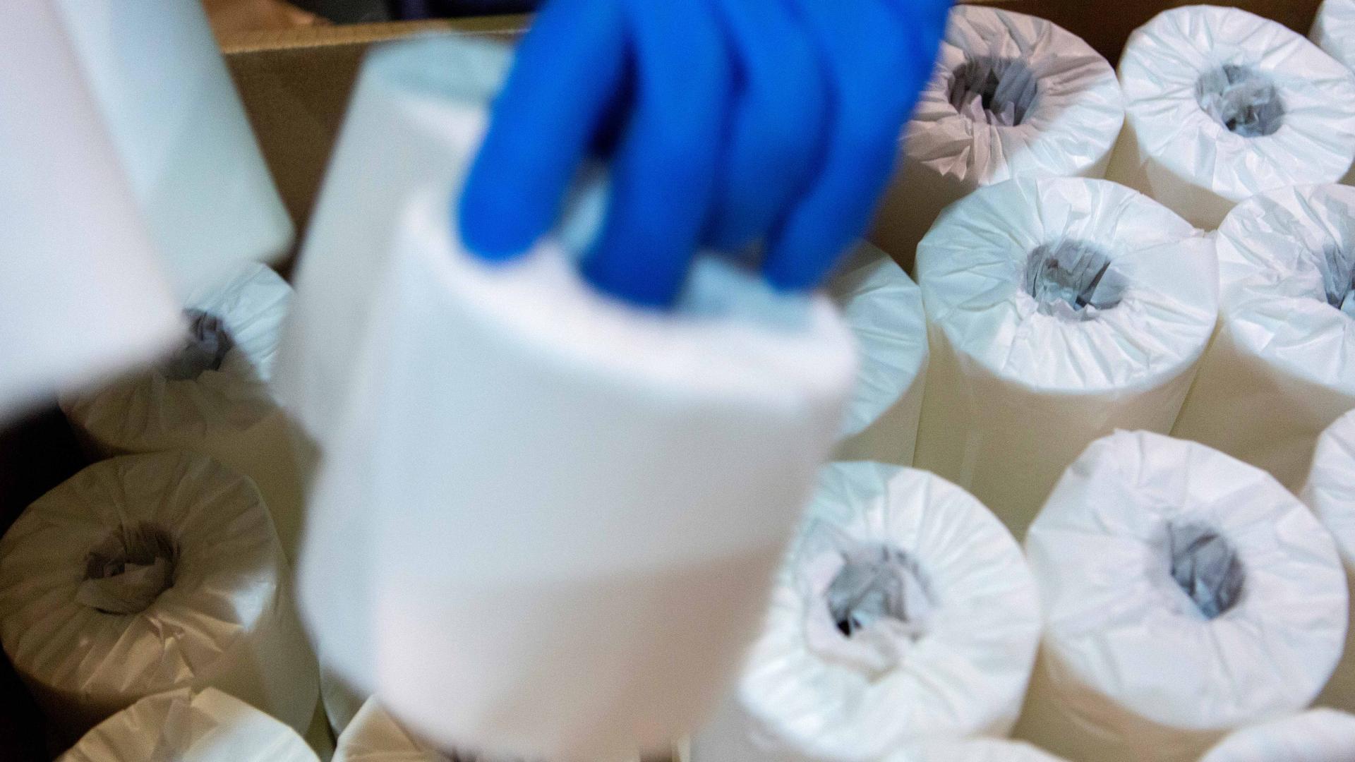 A close-up of the blue-gloved hand of a toilet paper packer who is boxing rolls of individually wrapped toilet paper to be shipped in Bangor, Maine, on April 7, 2020.