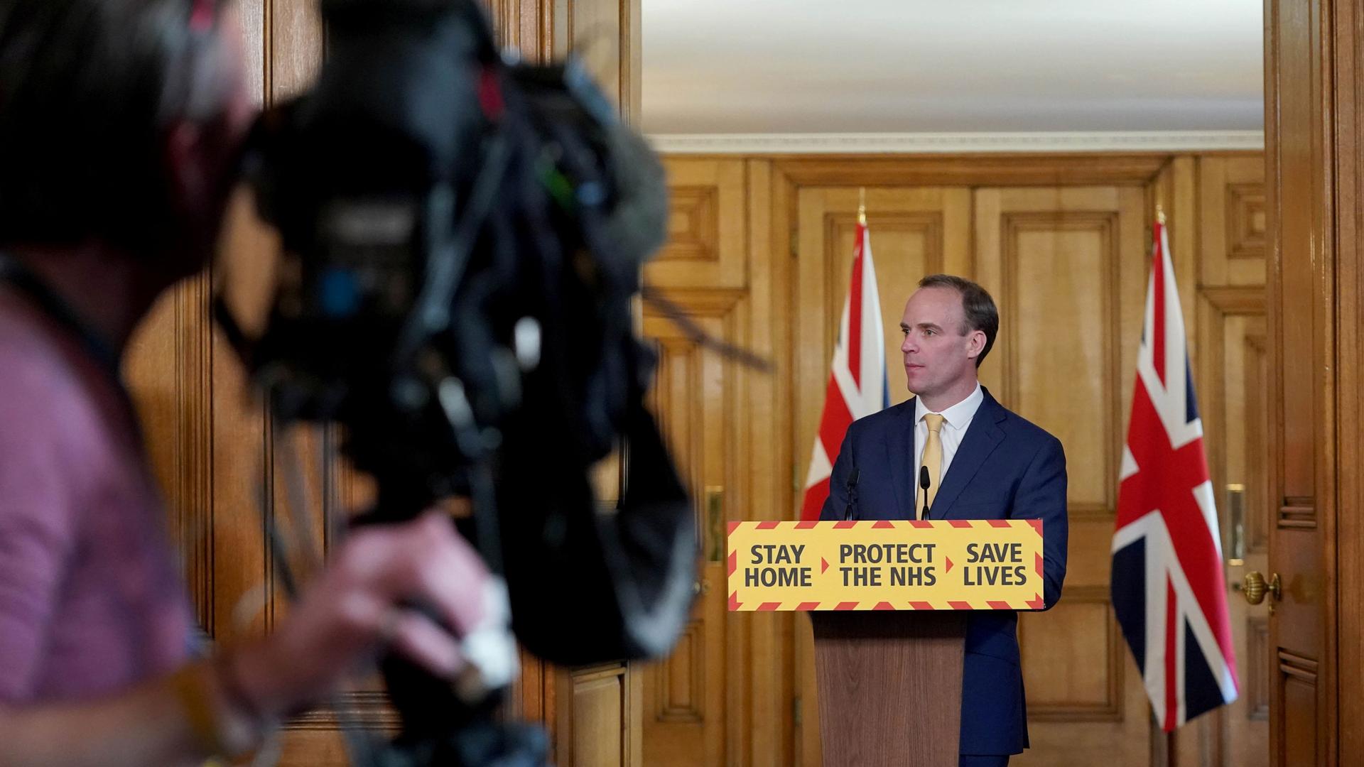 Britain's Foreign Secretary Dominic Raab is shown standing behind a podium witth the words, 