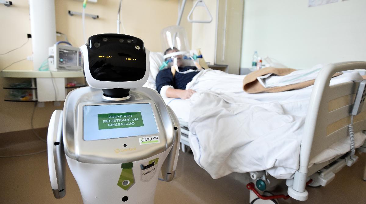 A picture of a robot in a hospital room and a patient laying on the bed sick.