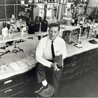 A black and white photograph of Cal-Tech scientist Arie Haagen-Smit who is standing with one foot on a stool in a laboratory.