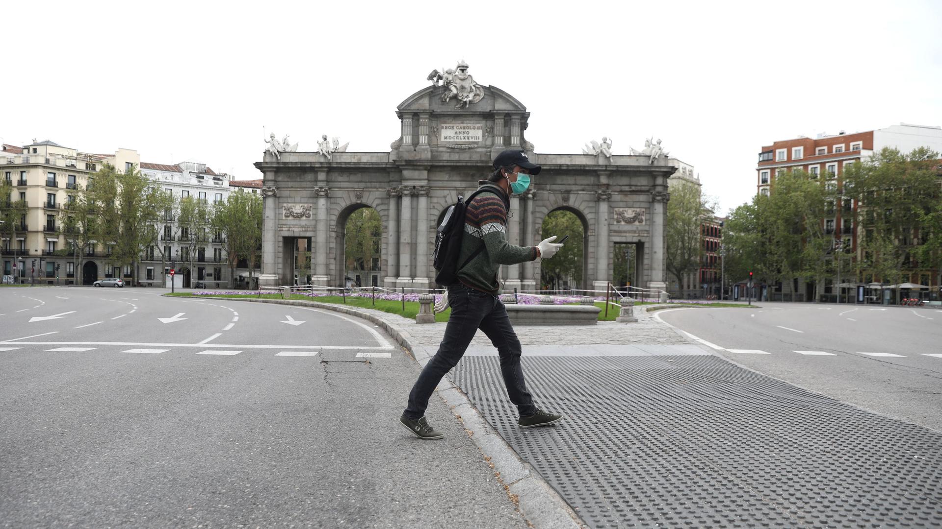 A man wearing a protective face mask and gloves walks past the empty landmark Alcala Gate