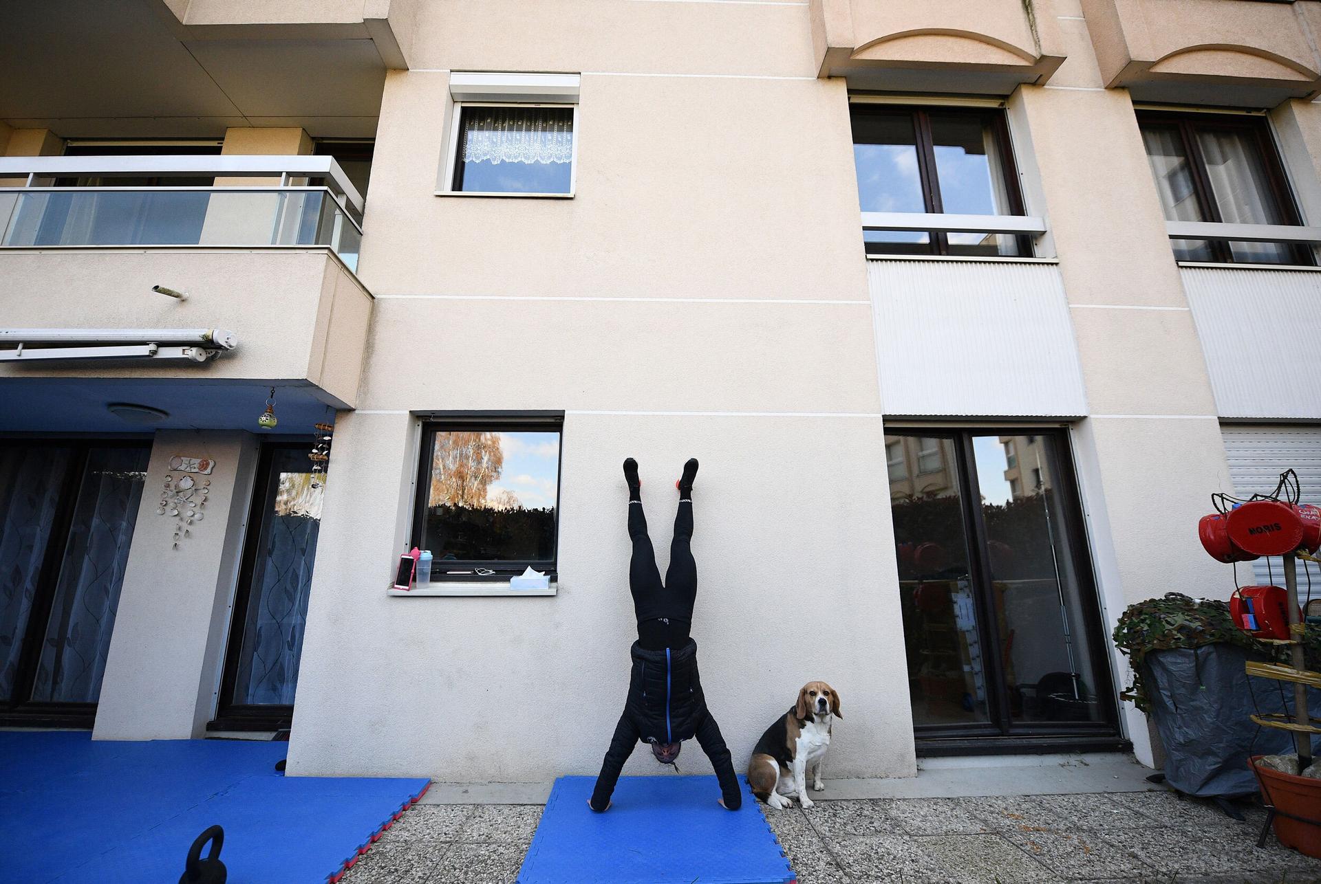 A woman on black gym clothes does a hand-stand on a mat in her backyard.