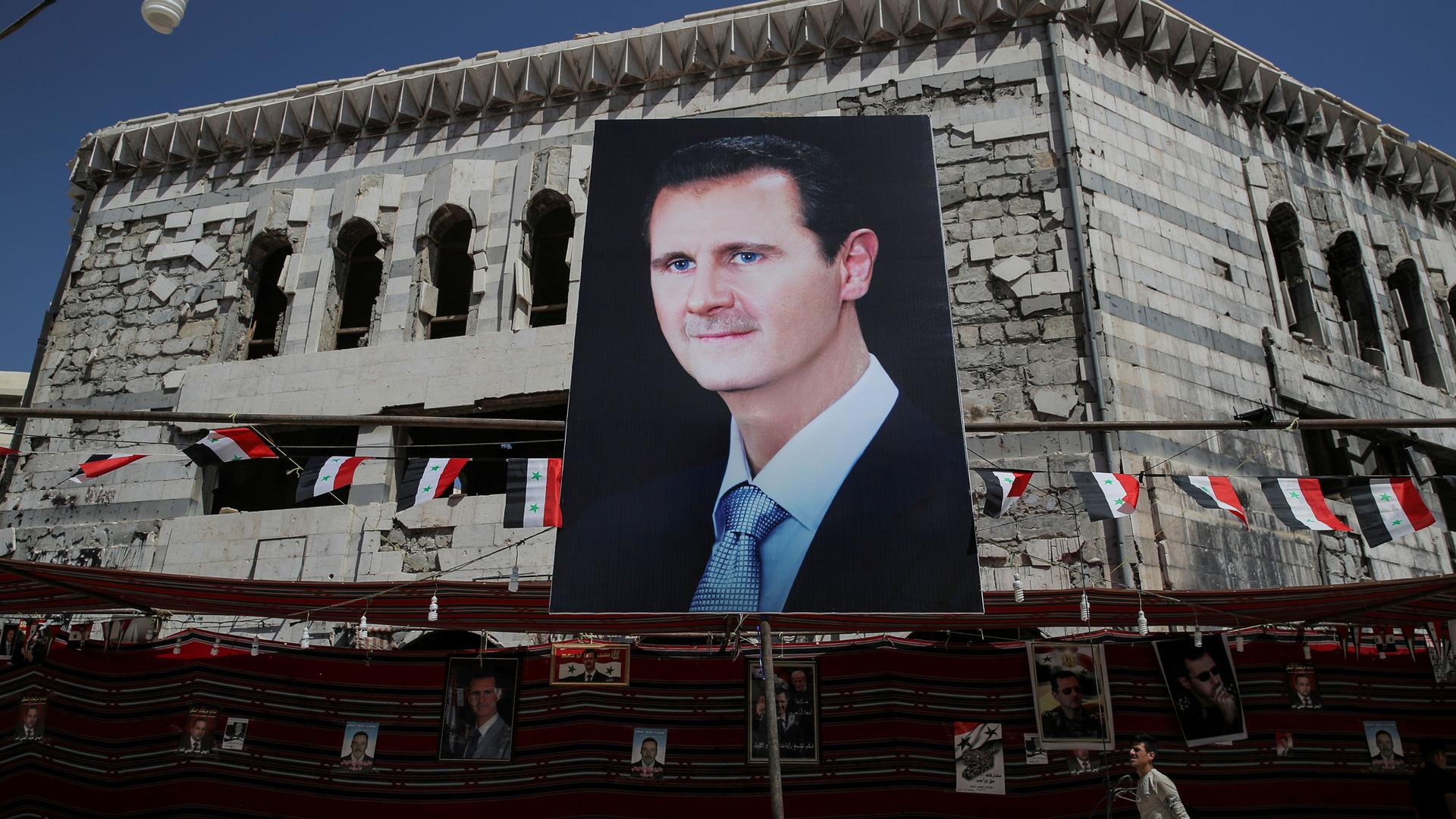 A large portrait photograph is show of Syrian president Bashar al-Assad with several Syrian flags flying behind it.