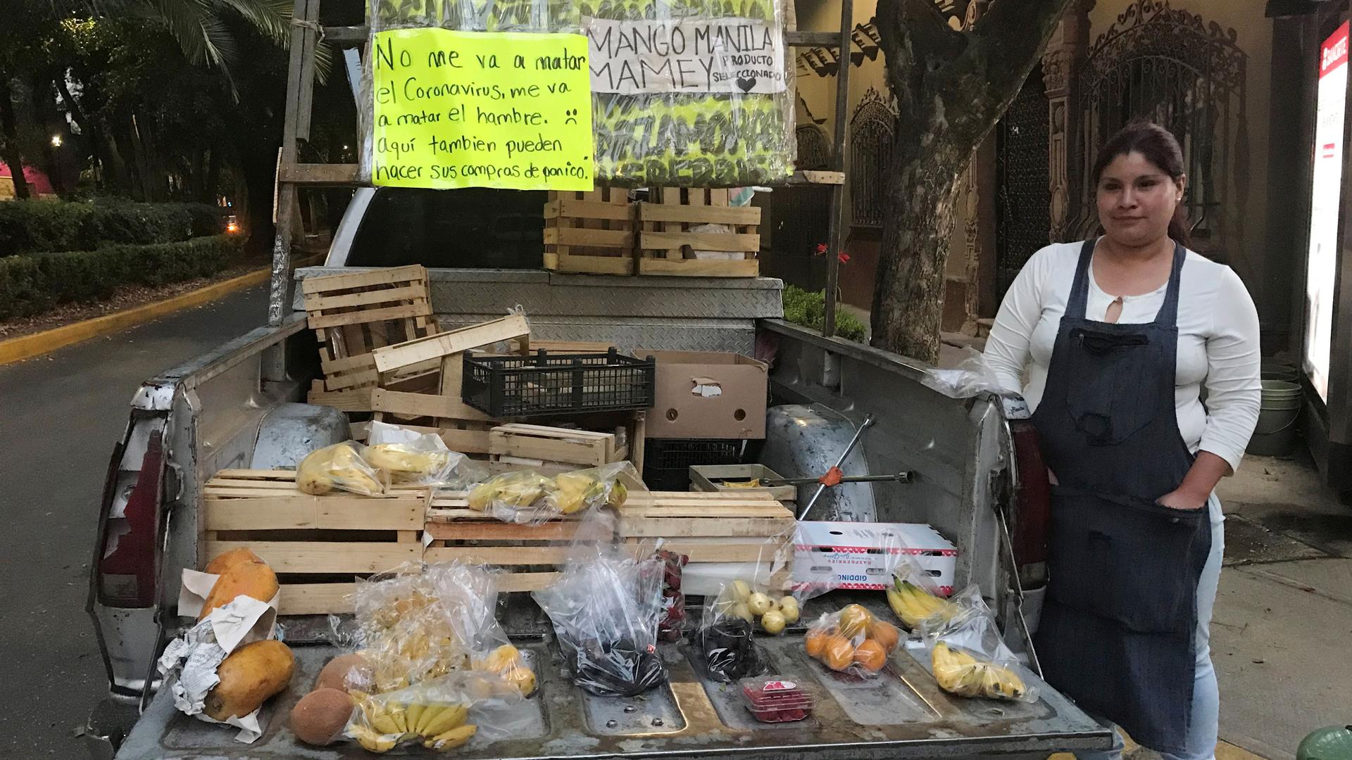 A woman stands by a display of fruit