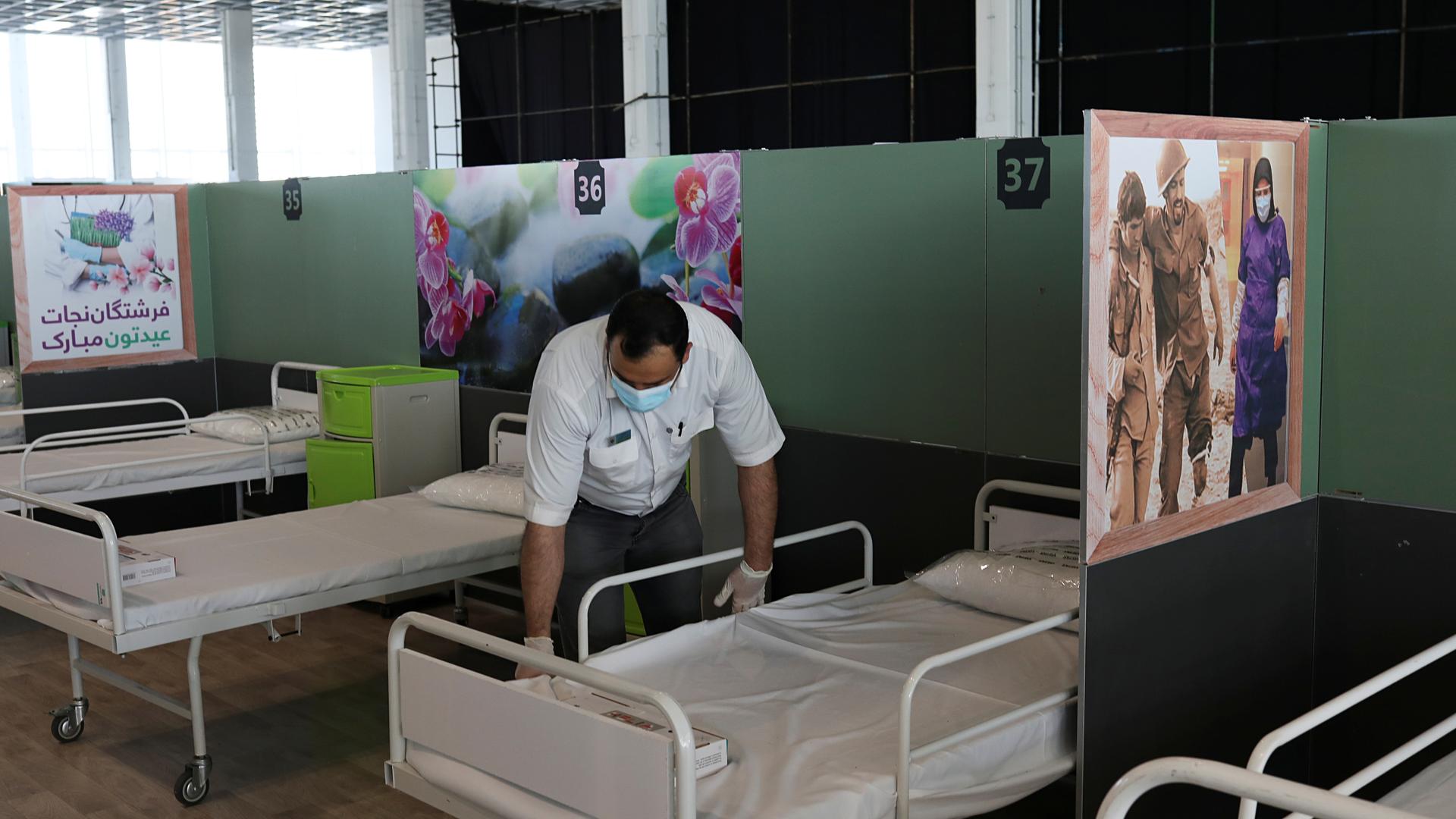 A man makes a bed in a row of beds with medical posters on the dividing walls 