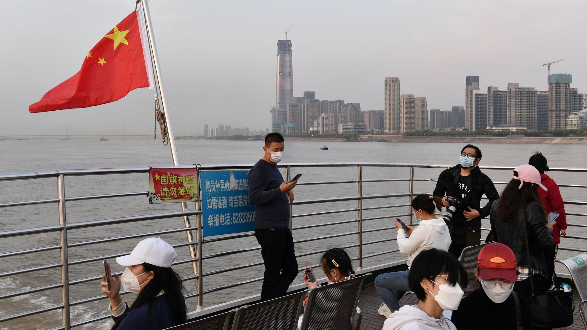 People in face masks ride on a ferry with a Chinese flag