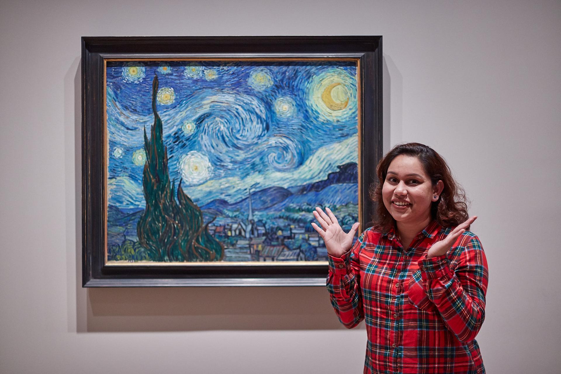 A woman in a red-checkered shirt poses in front of Vincent van Gogh's famous painting, 
