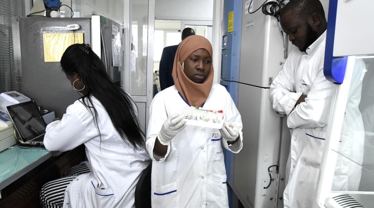 A woman in a white robe carries some lab material inside lab in Senegal.