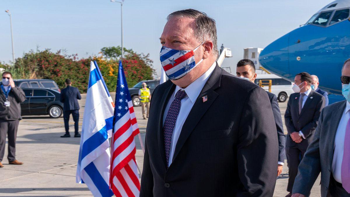 Mike Pompeo in a suit and face mask in front of a plane and the US and Israeli flags