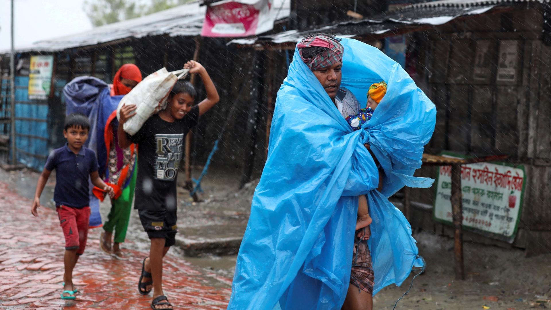 A man is shown wrapped in a blue tarp followed by several other people as heavy rains from Cylone Amphan fall.