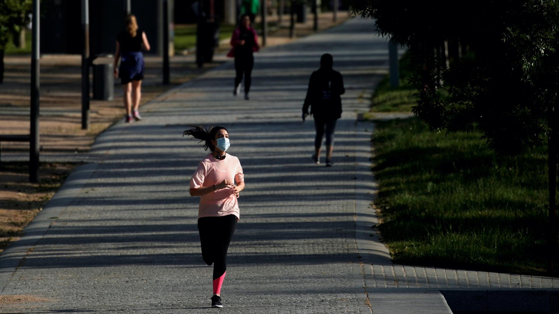 A woman wearing a protective face mask runs in Madrid Rio park, during the hours allowed for individual exercise. 