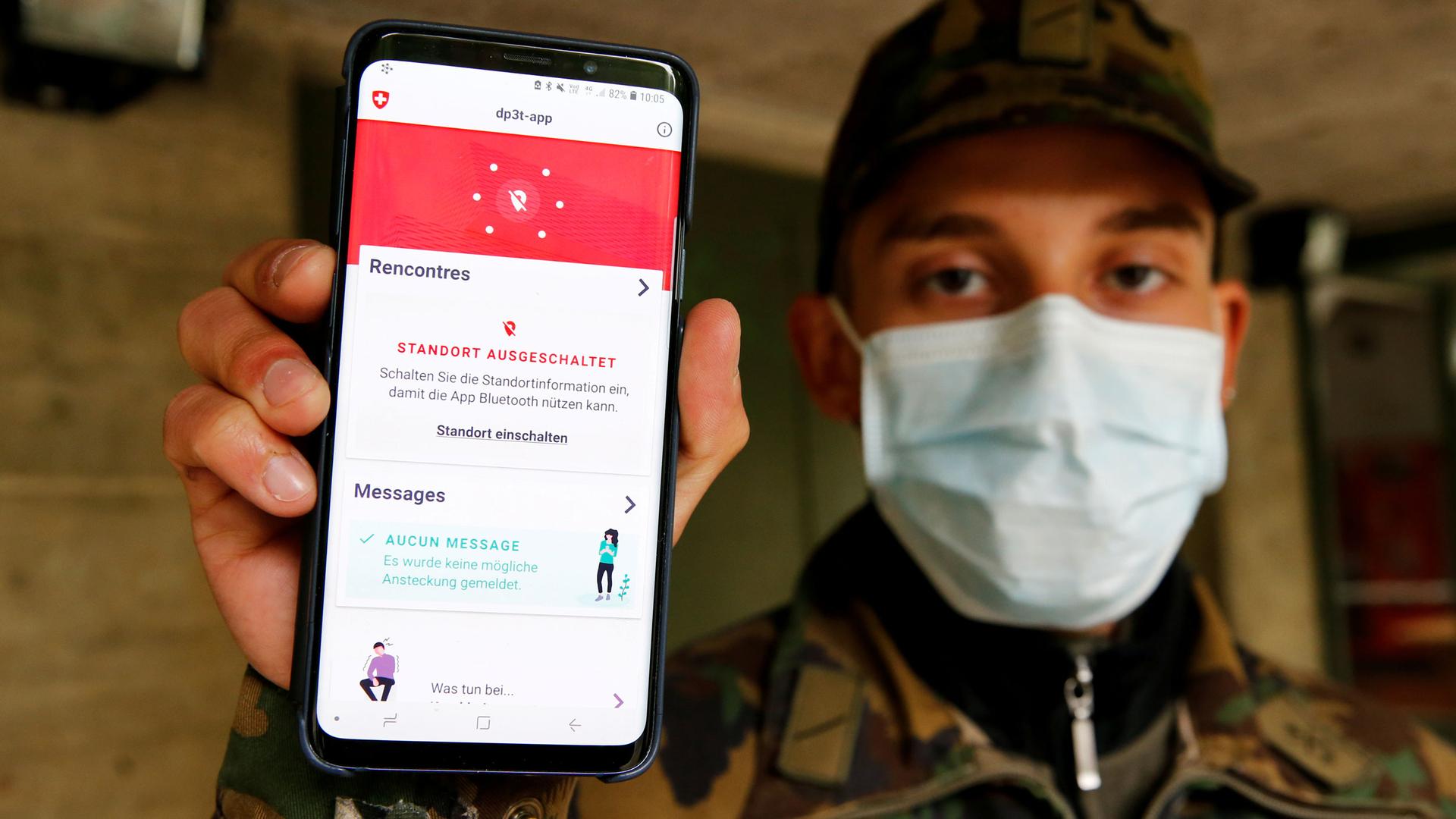 A man in fatigues and a face mask holds a phone with an app to the camera