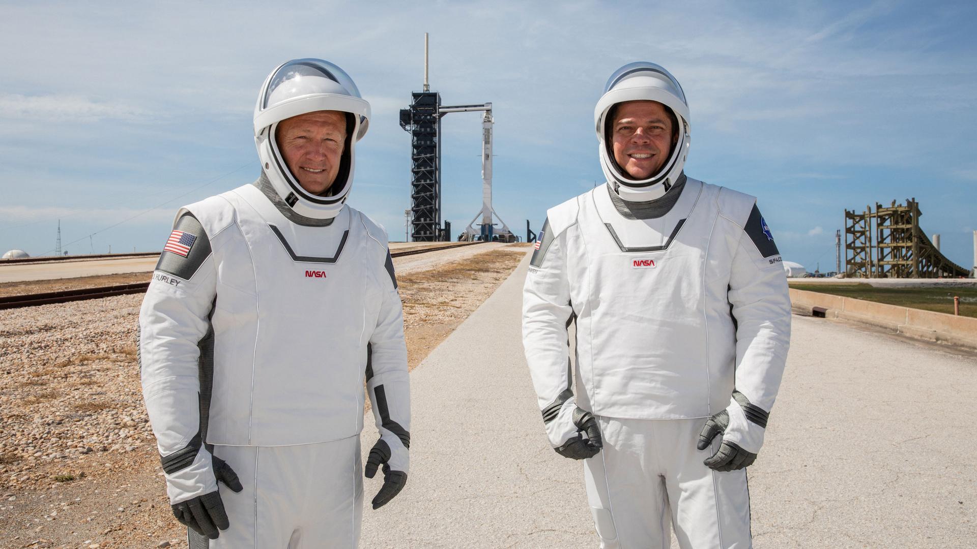 Two NASA astronauts in spacesuits in front of a rocket launch pad