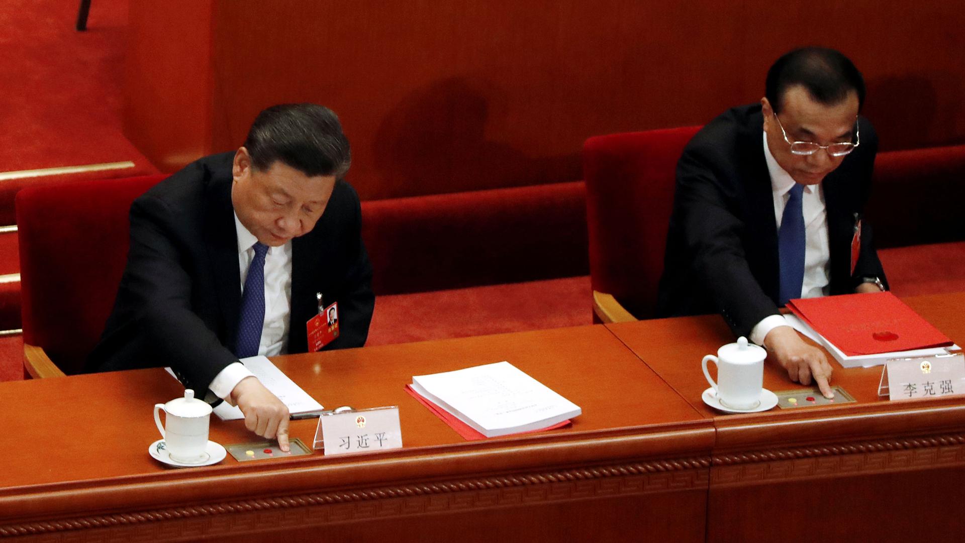Chinese President Xi Jinping and Premier Li Keqiang are shown sitting in red chairs and pressing buttons in front of them to cast their vote.