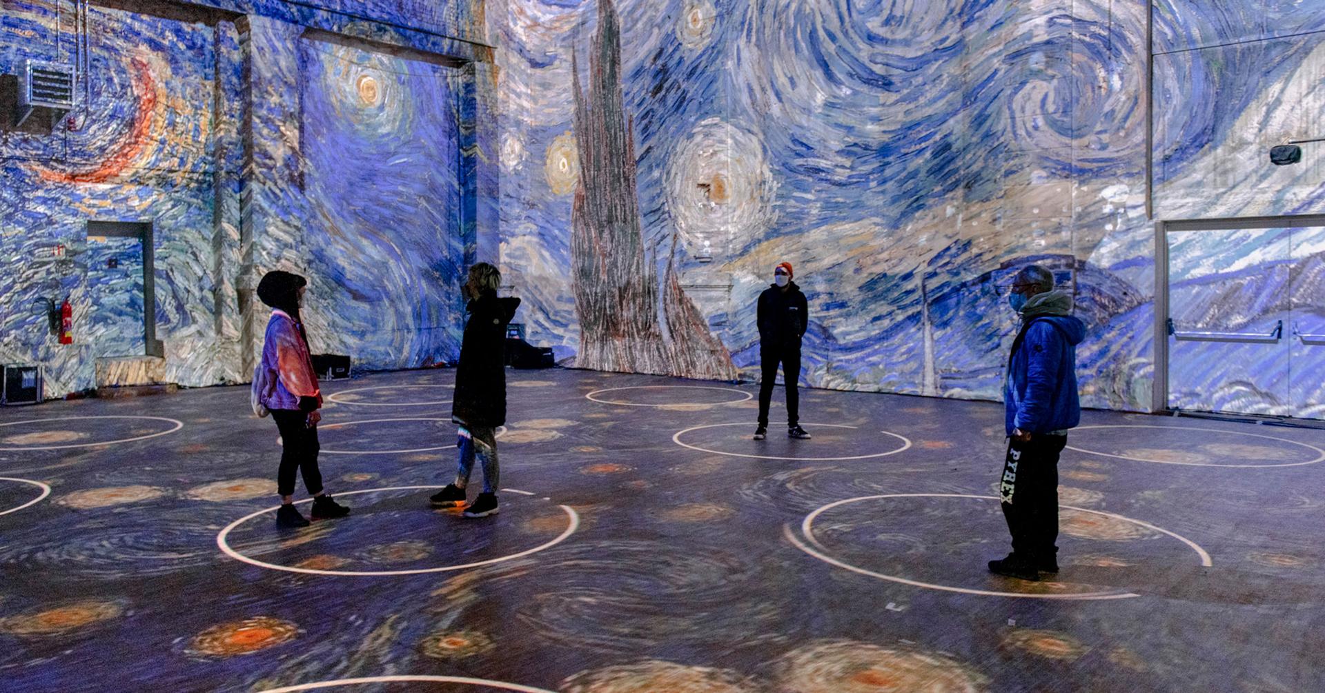 A photo mock up of Van Gogh art projected in a space with people standing in 