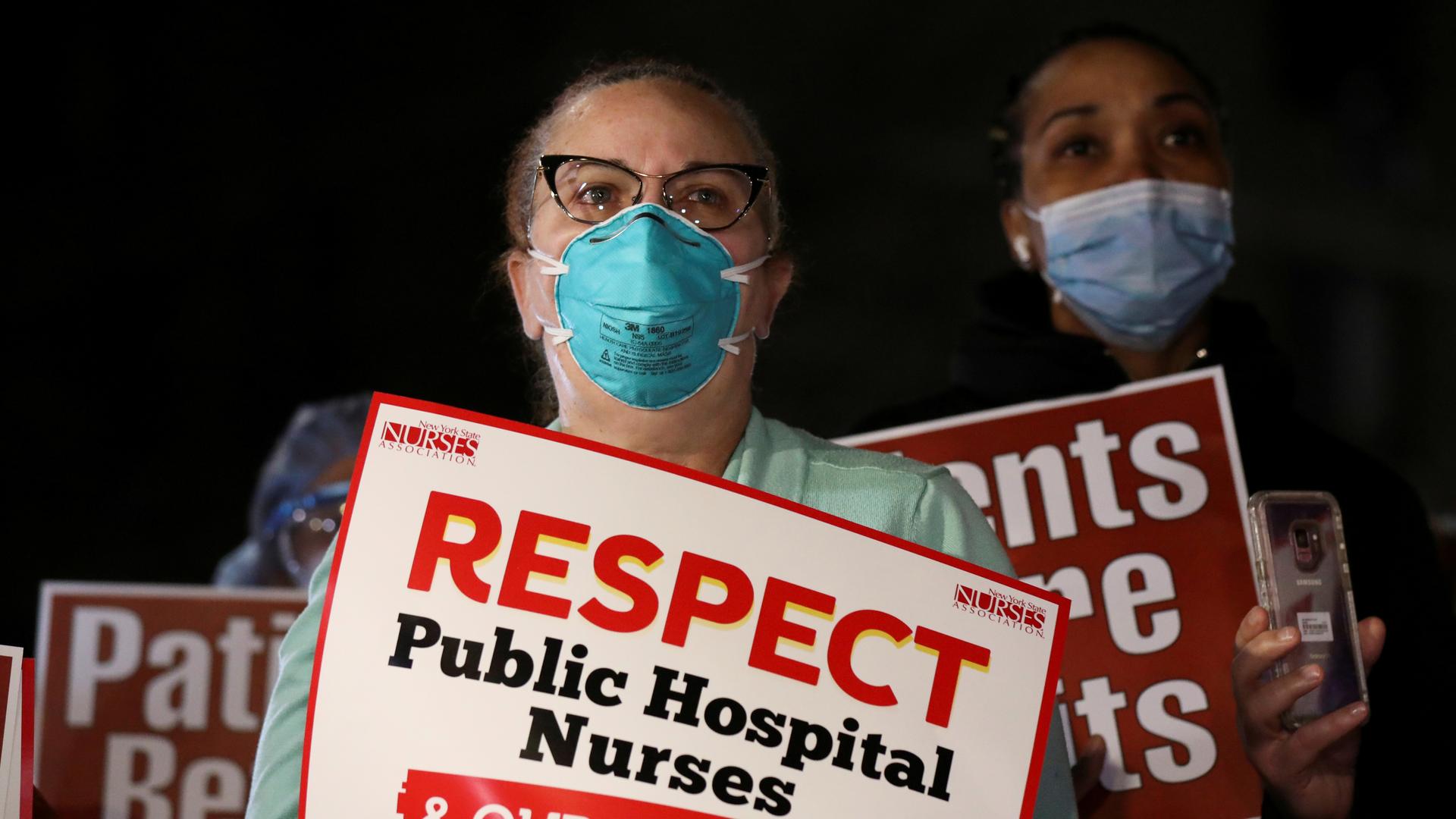 Two women stand with protest signs about respecting nurses