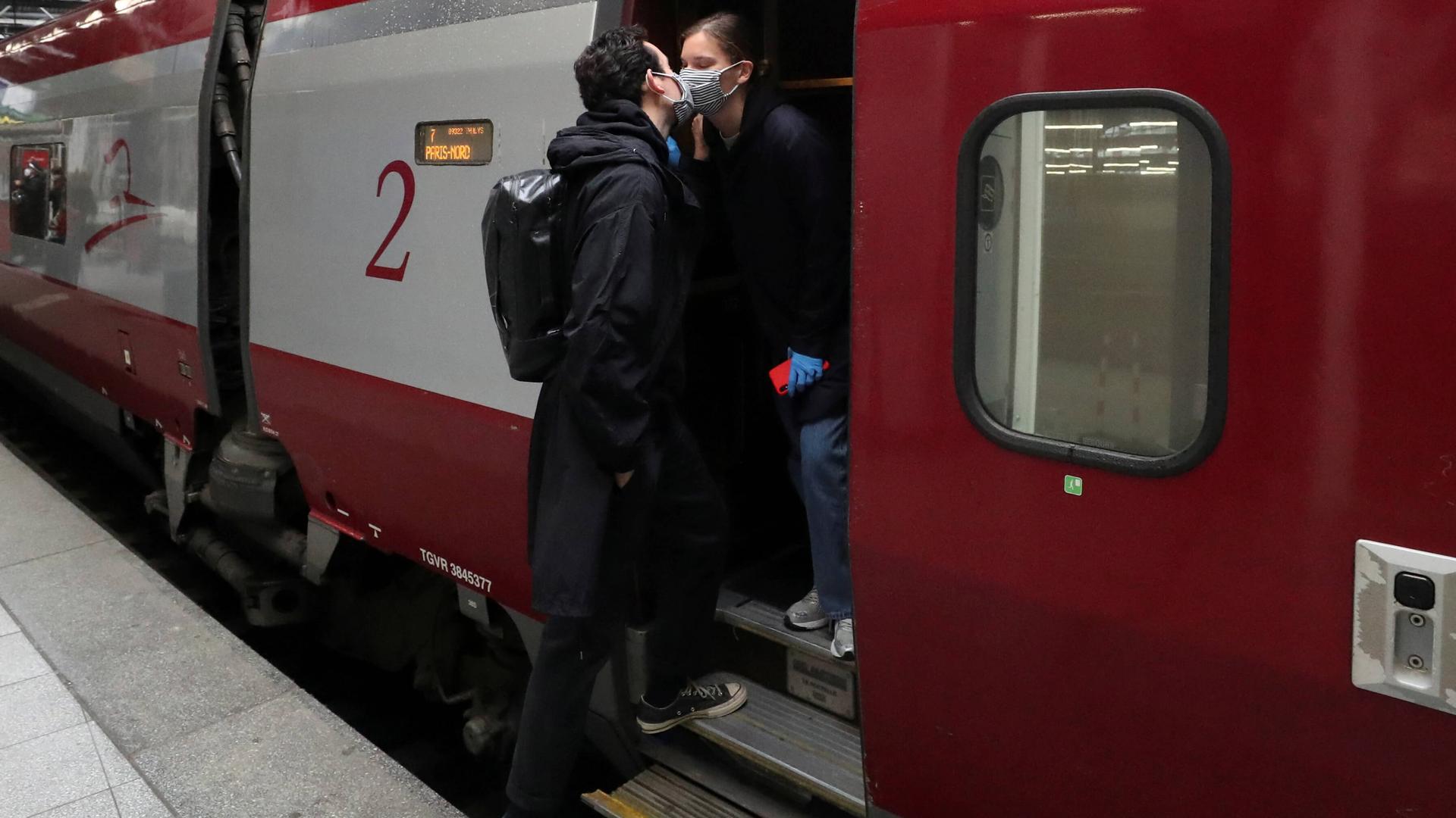 Two people kiss wearing face masks as they board a train