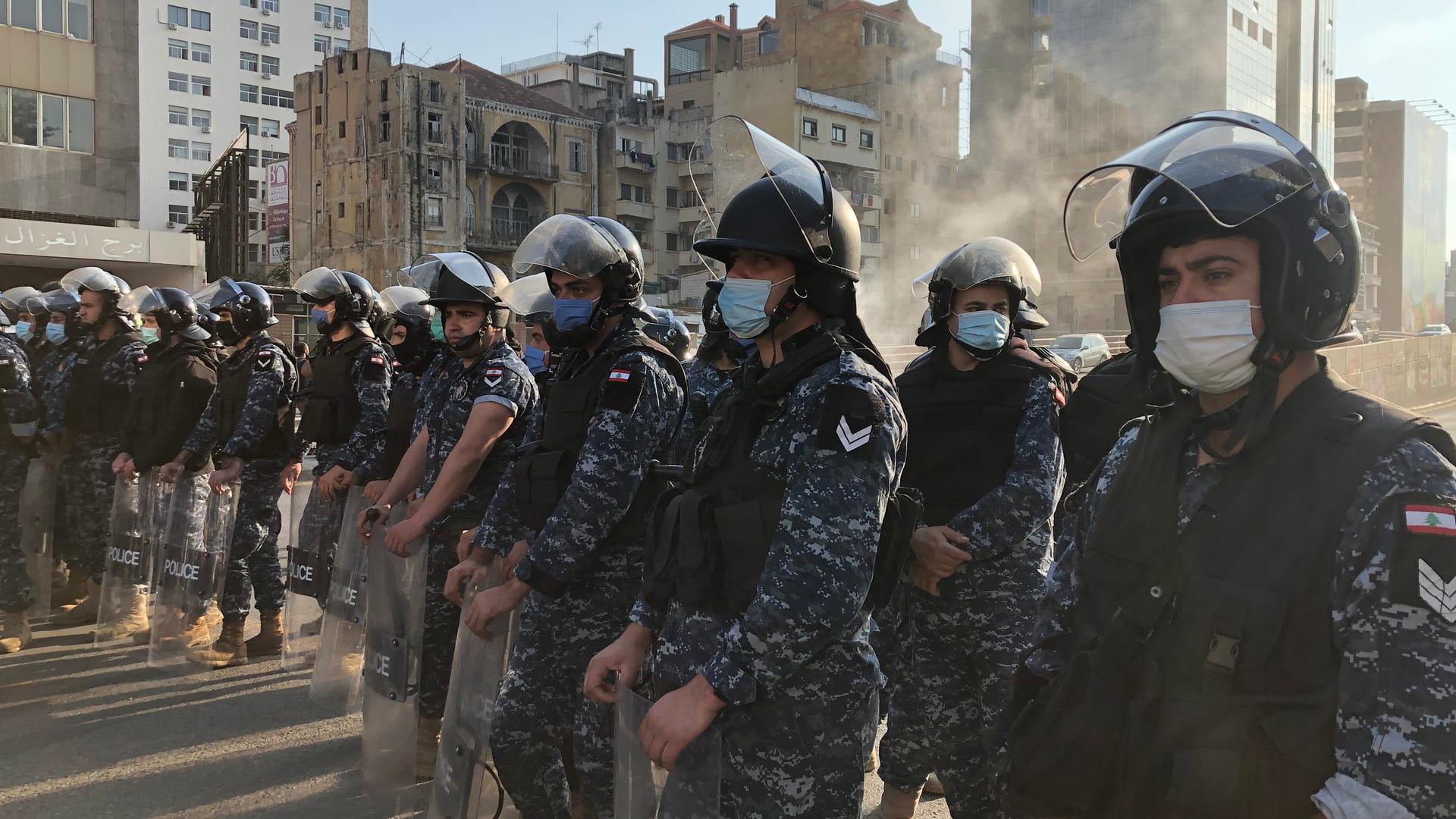 People in military uniform wear face masks while they form a line on a Beirut street during protest. 