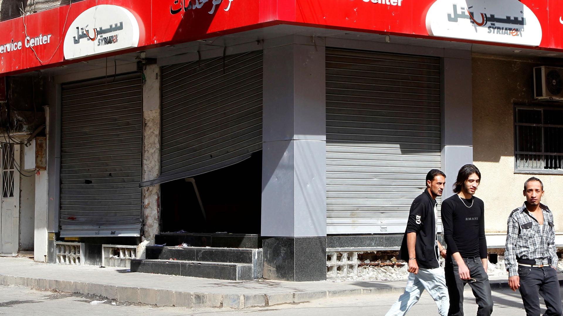 People walk past the looted premises of cellphone company Syriatel, which is owned by Rami Makhlouf, the cousin of Syria's President Bashar al-Assad, in Deraa March 21, 2011. 