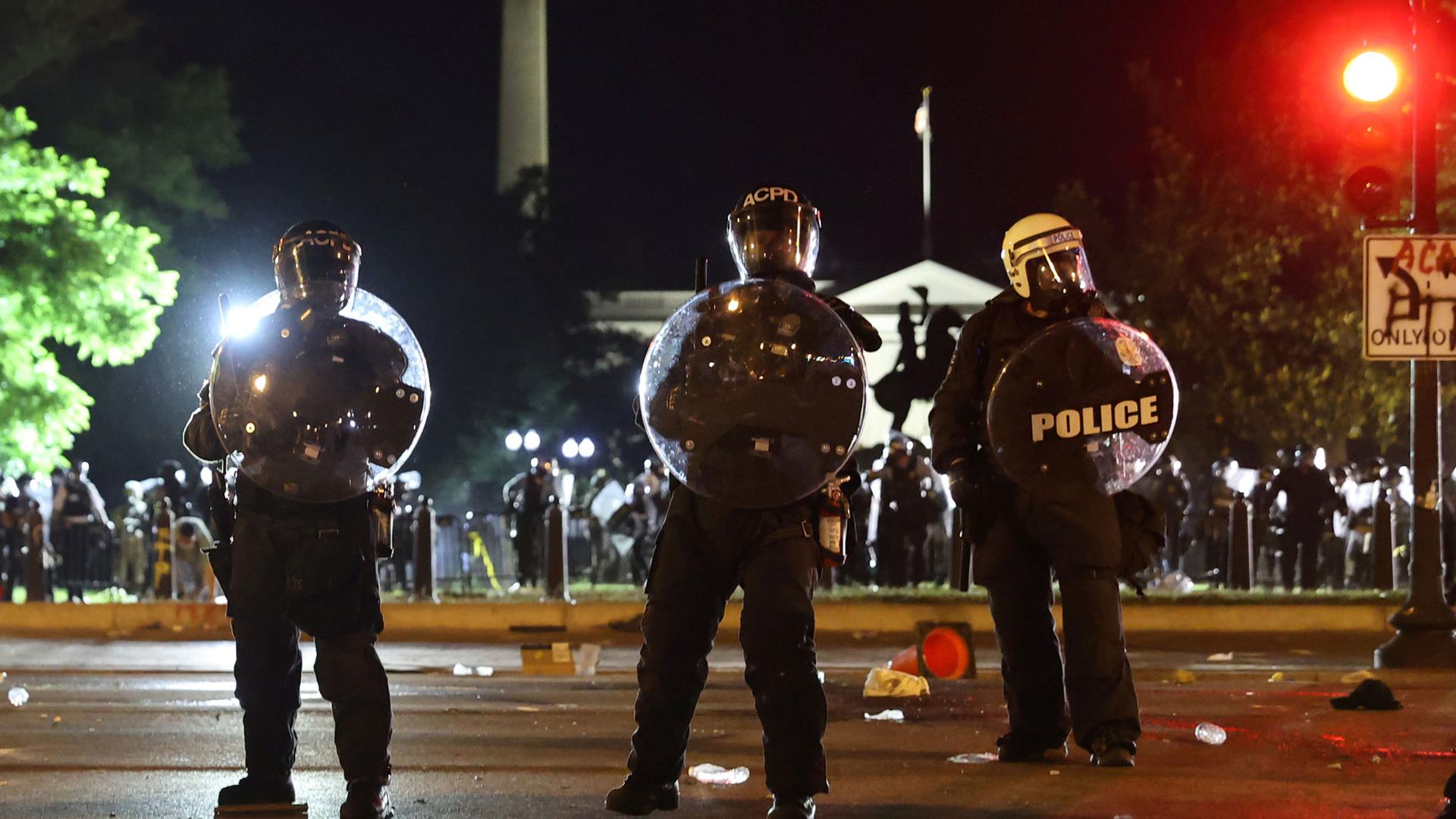 Several police officers are shown carrying shields and wearing riot gear with the White House in the background.