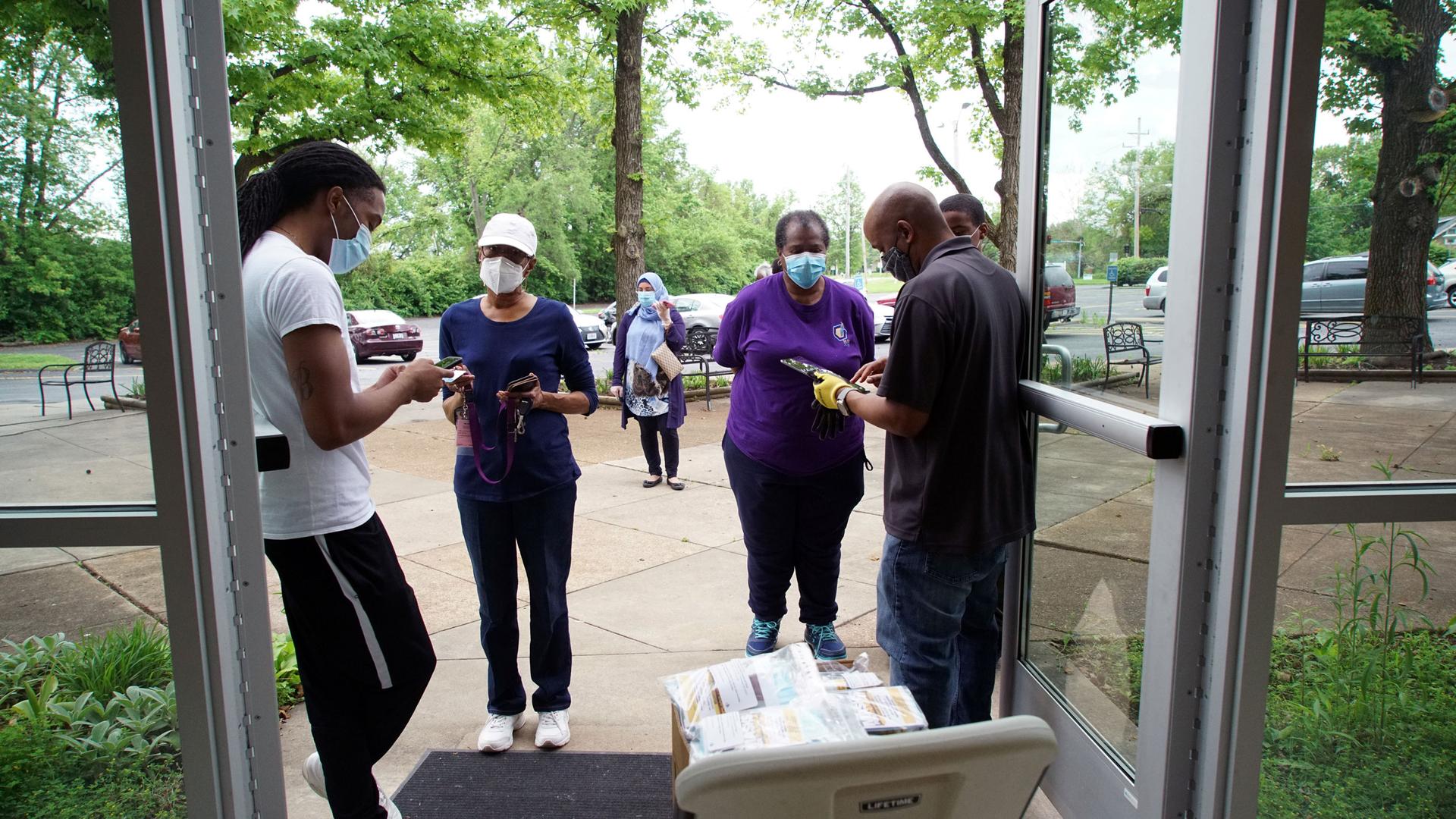 Several Black people stand around double doors in masks handing out supplies