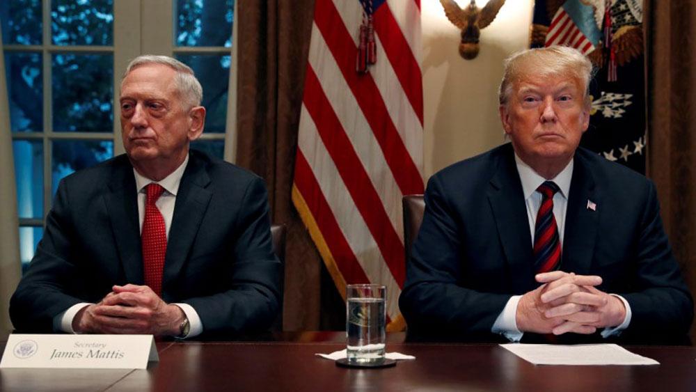 US President Donald Trump is shown sitting at a wooden table next to then Defense Secretary James Mattis with the US flag behind them.
