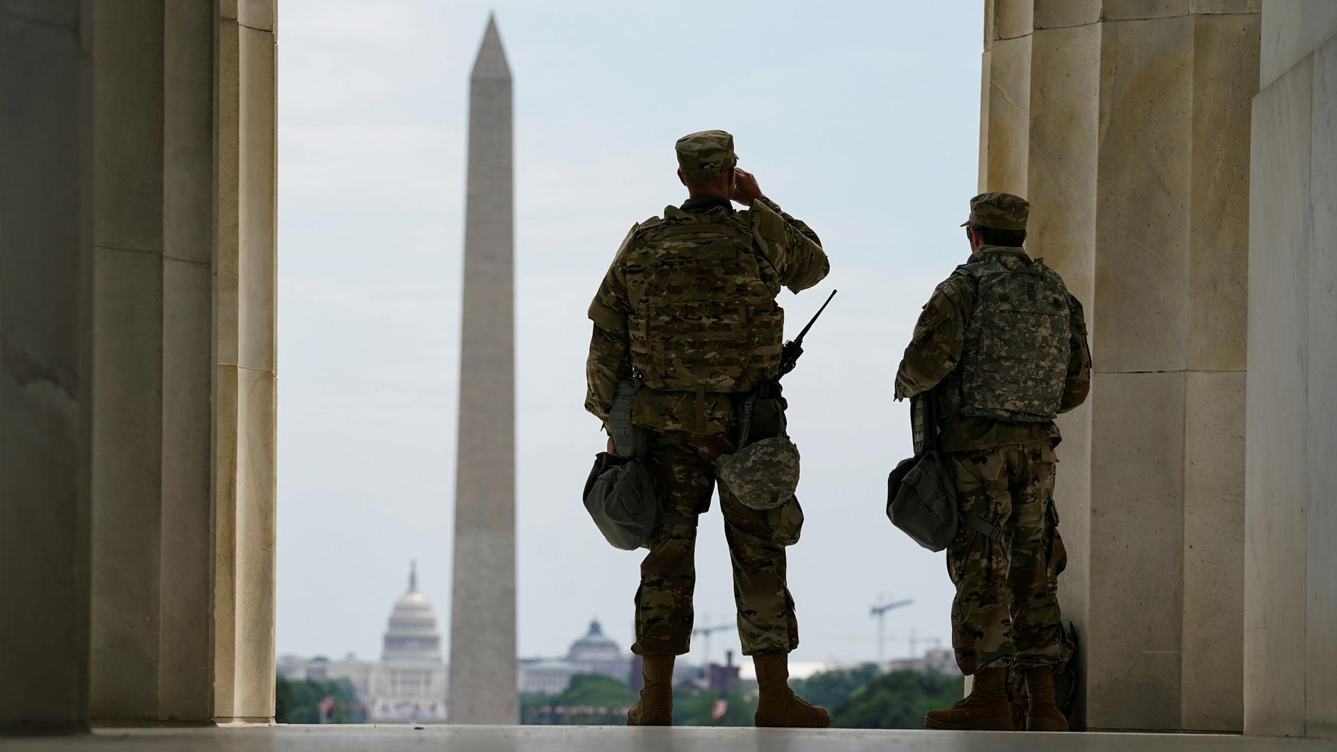 Two US soldiers are shown looking out at the Washington Monument with the US Capitol Building off in the distance.