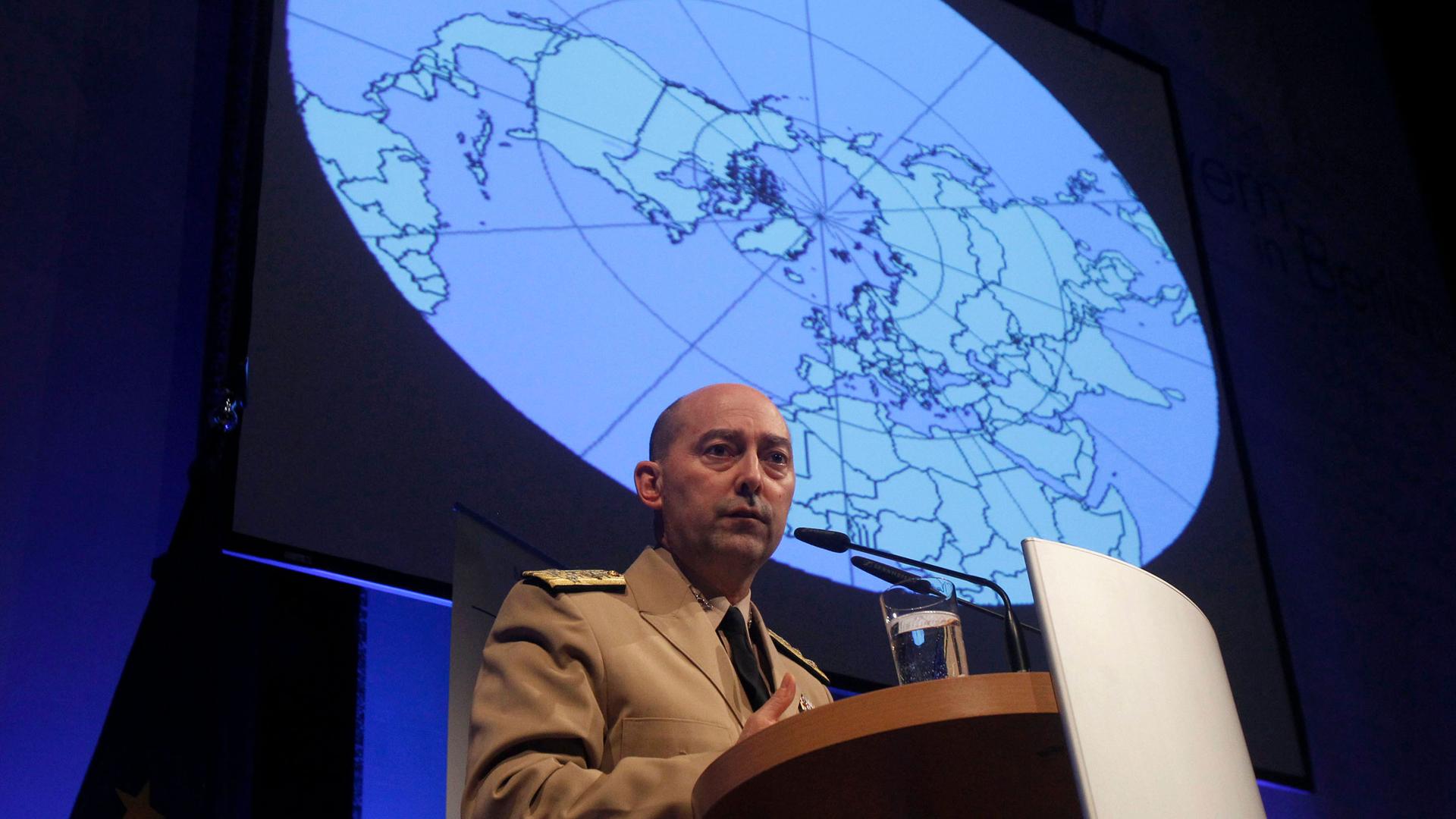 A man stands at a podium with an image of a globe behind him