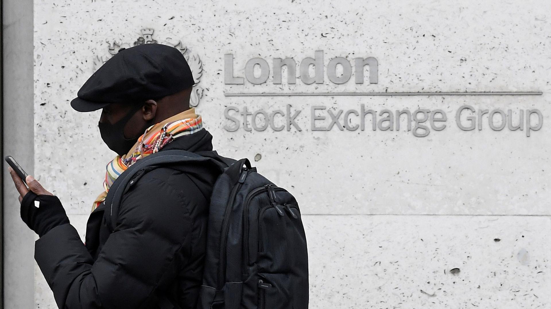A man wearing a protective face mask and hat walks past the London Stock Exchange Group building