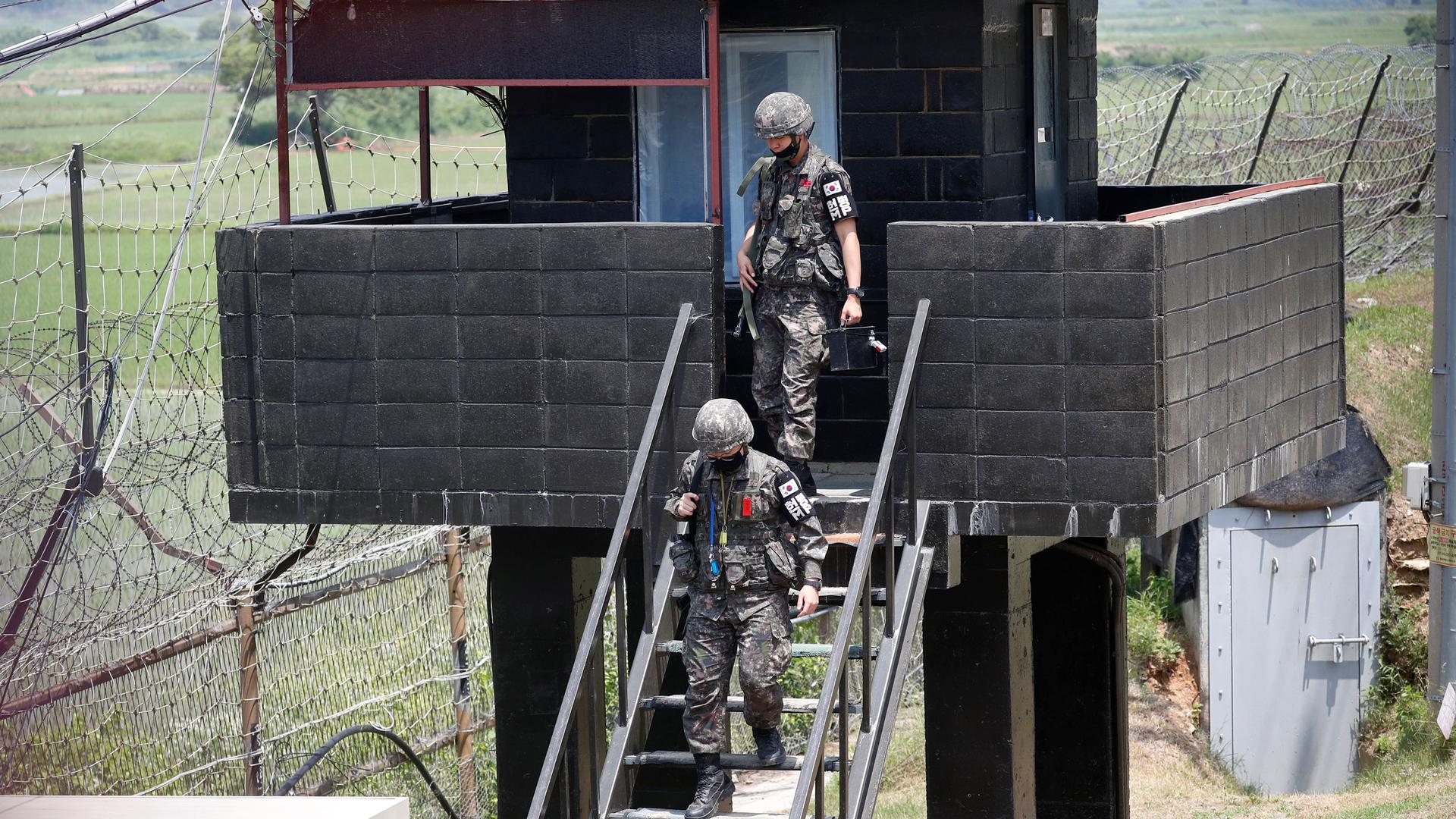 Two soldiers dressed in military fatigues and carrying weapons are shown decending a staircase from a guard tower.