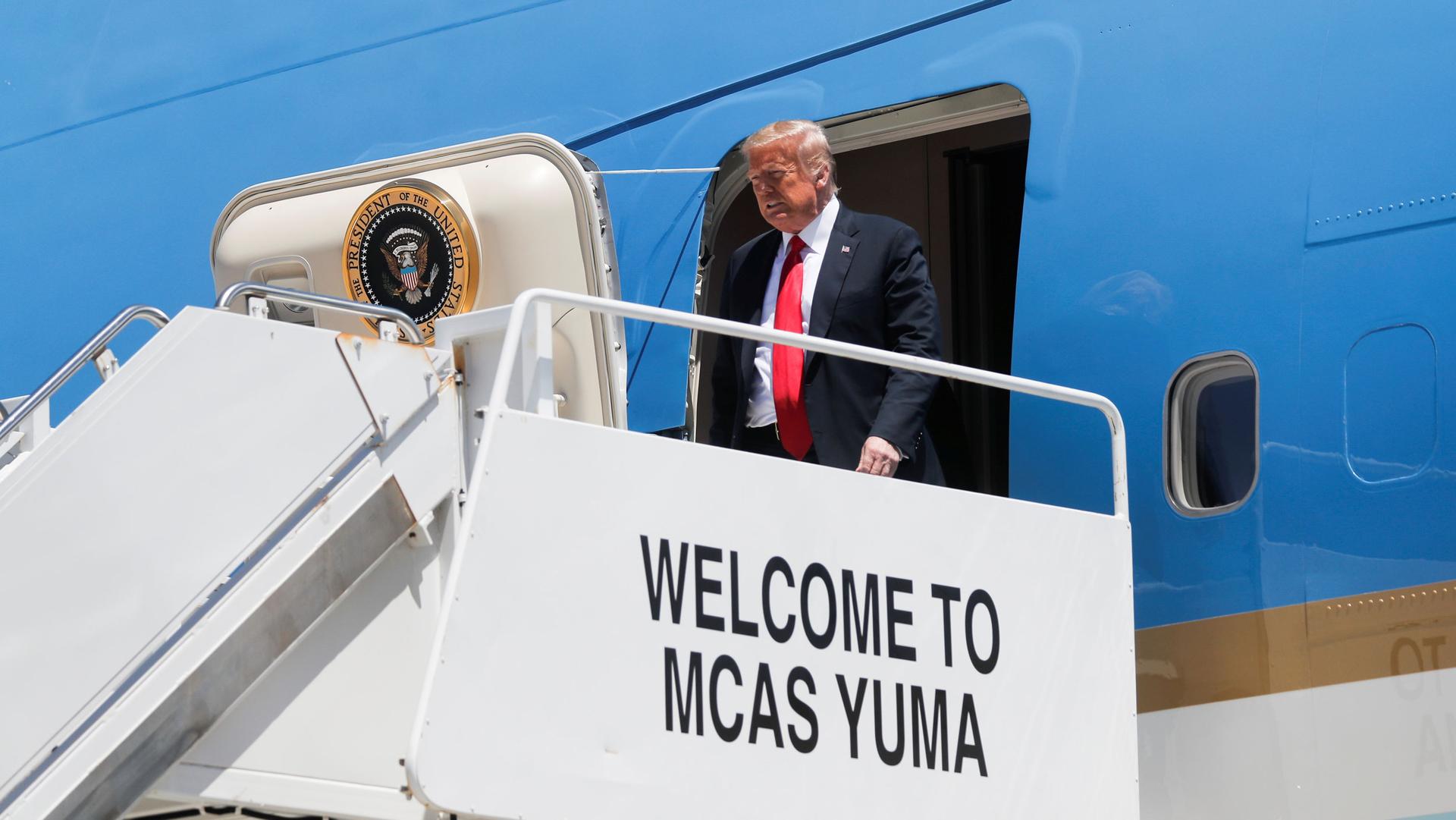 US President Donald Trump is shown exiting the blue-painted Air Force  One on a white platform with the words, 