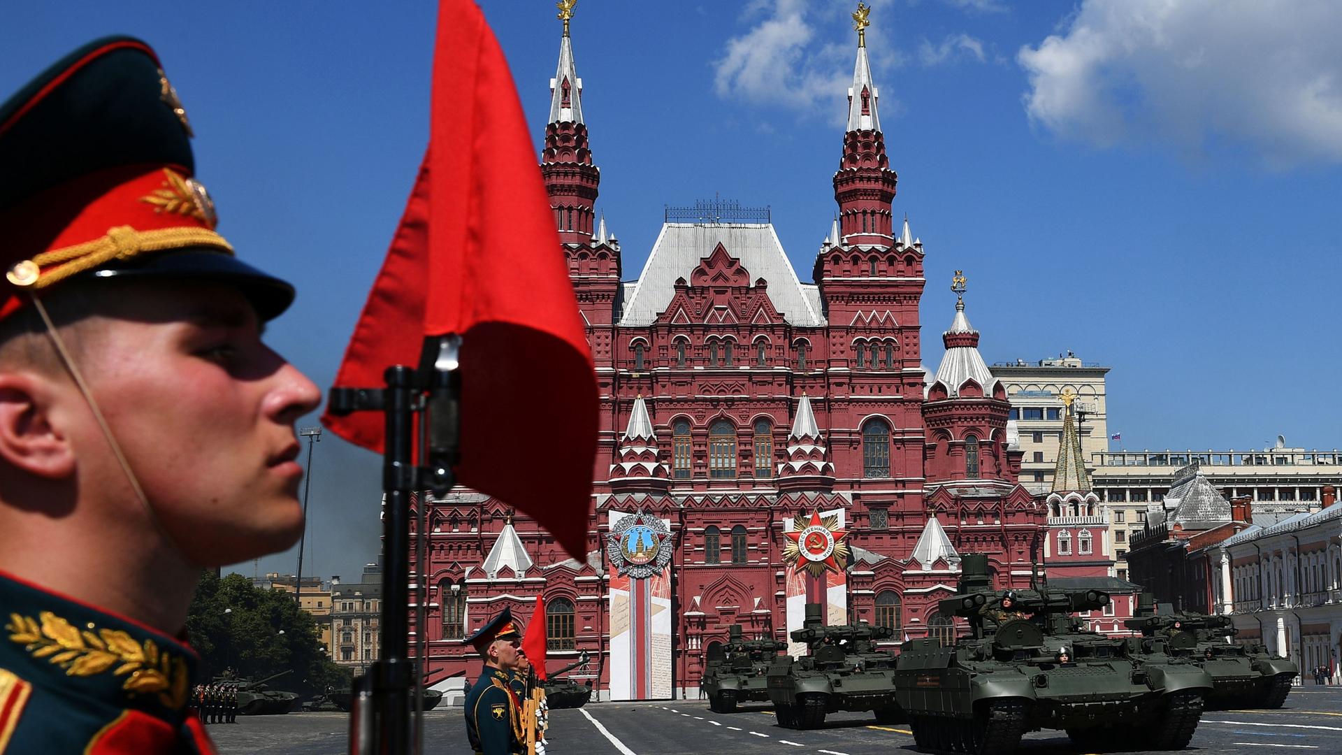 A close up of a man in uniform as tanks drive in Red Square in Moscow
