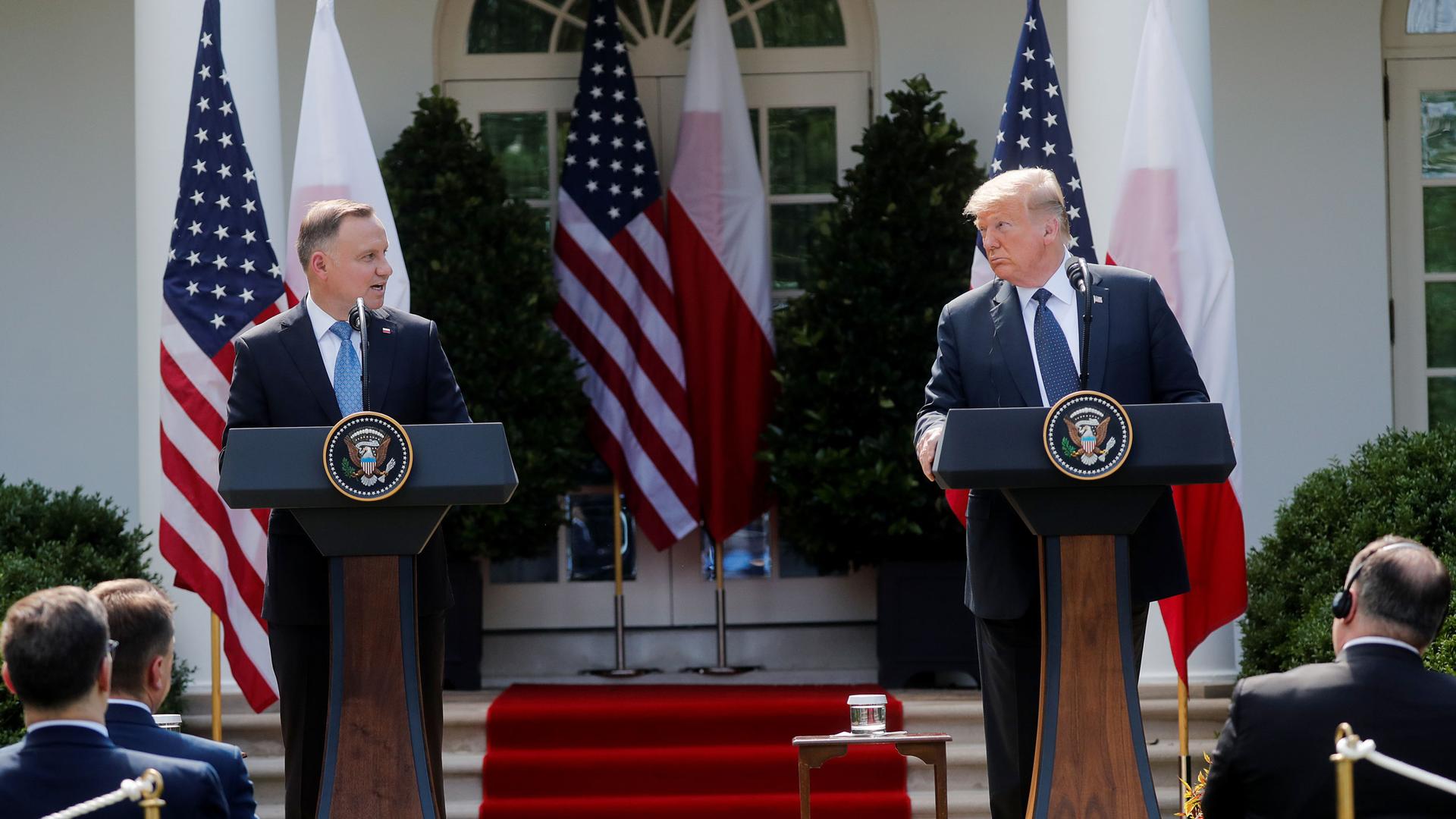 US President Donald Trump and Poland's President Andrzej Duda are shown standing at podiums across from each other with the White House in the background.