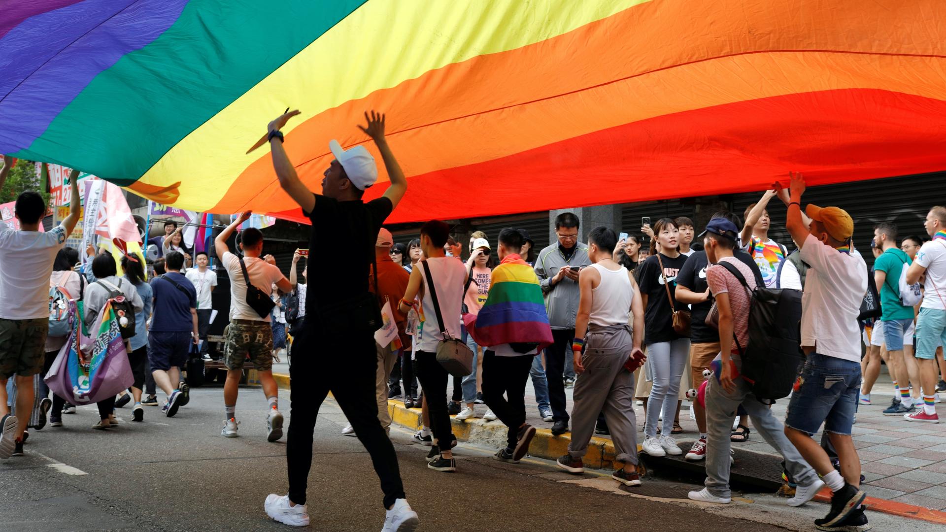 A group walks under a large rainbow flag. 