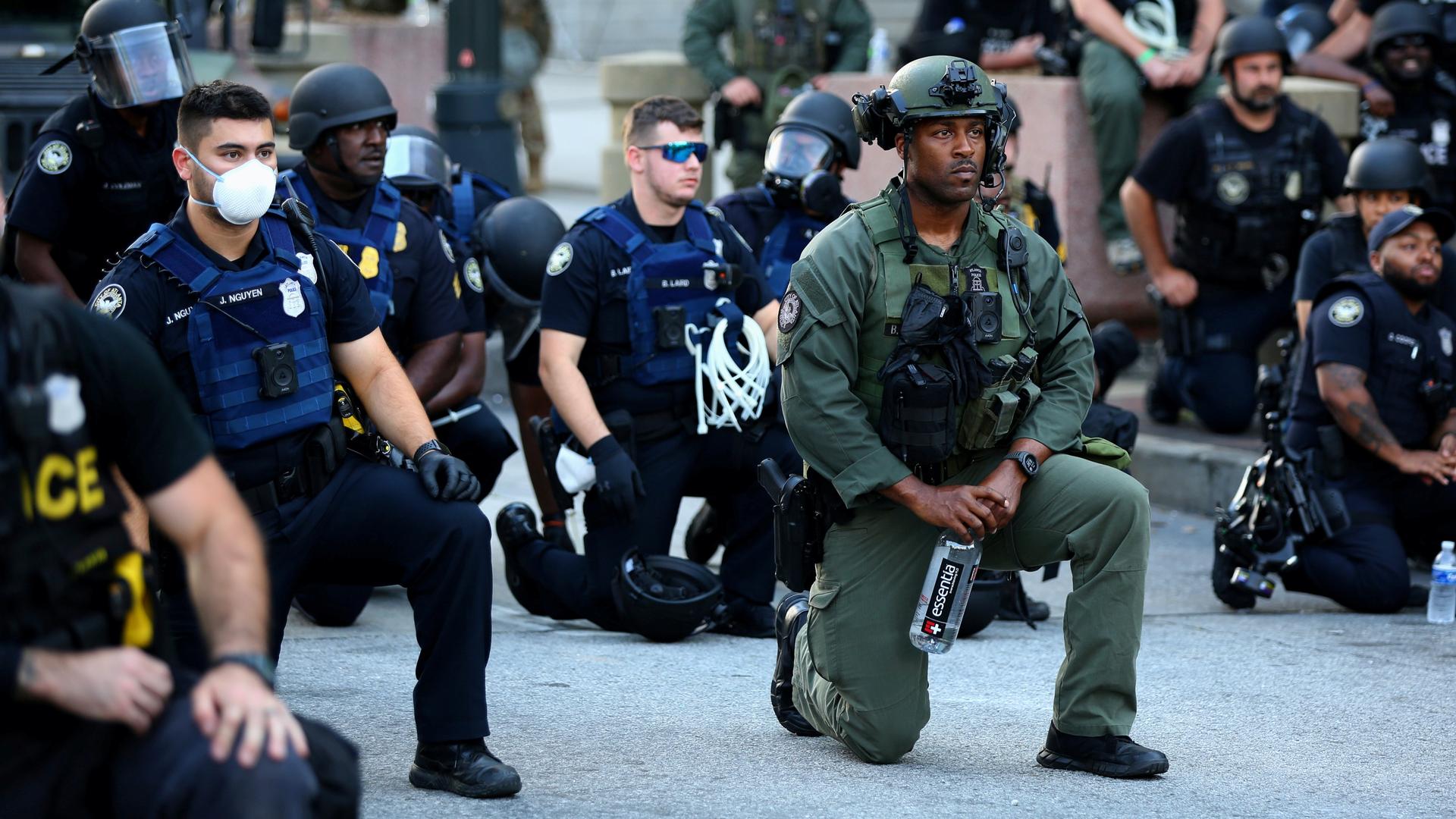Men in police uniform kneel on an urban street. 
