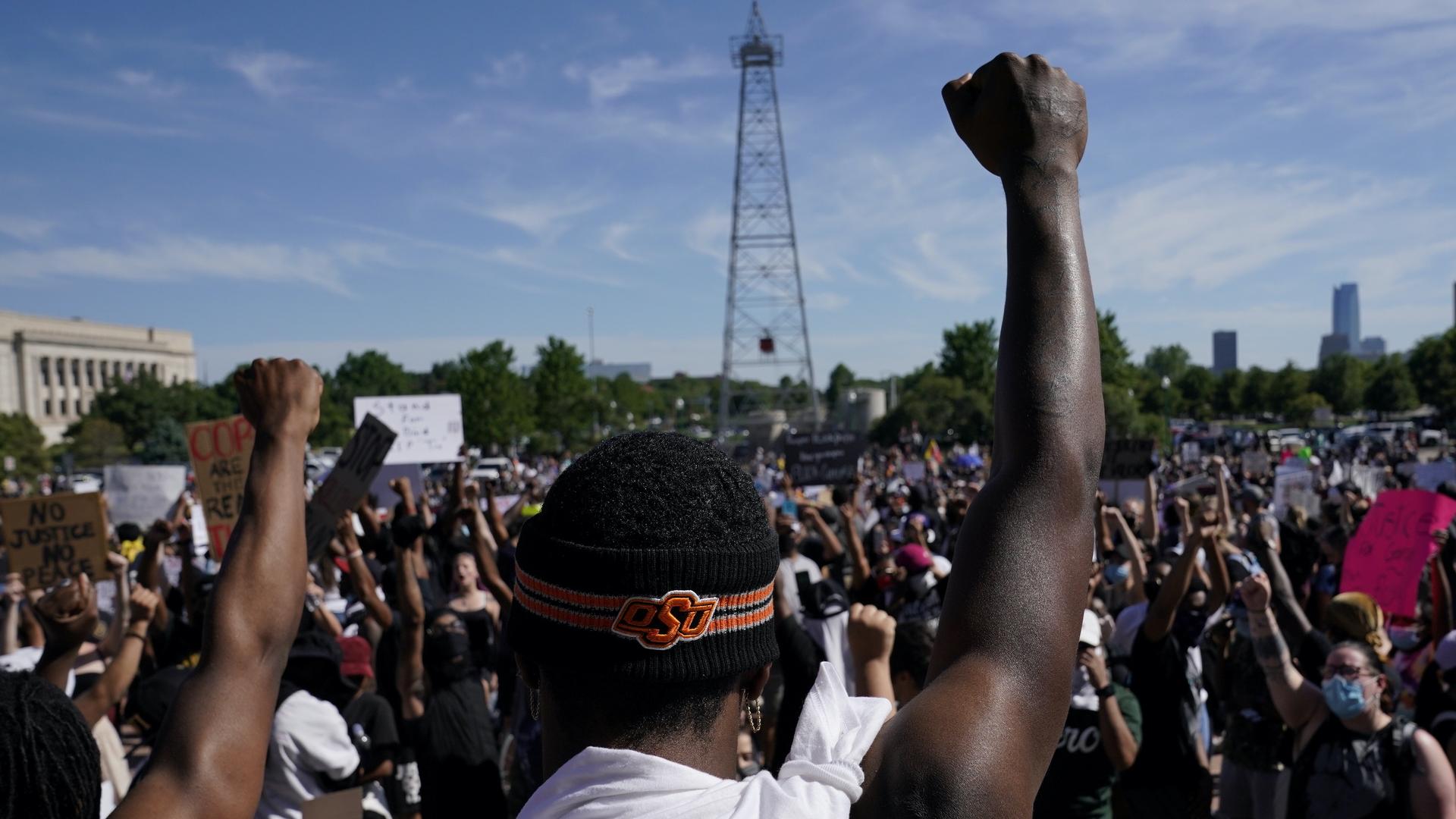 A black man stands in a crowd with his fist raised in the air. 