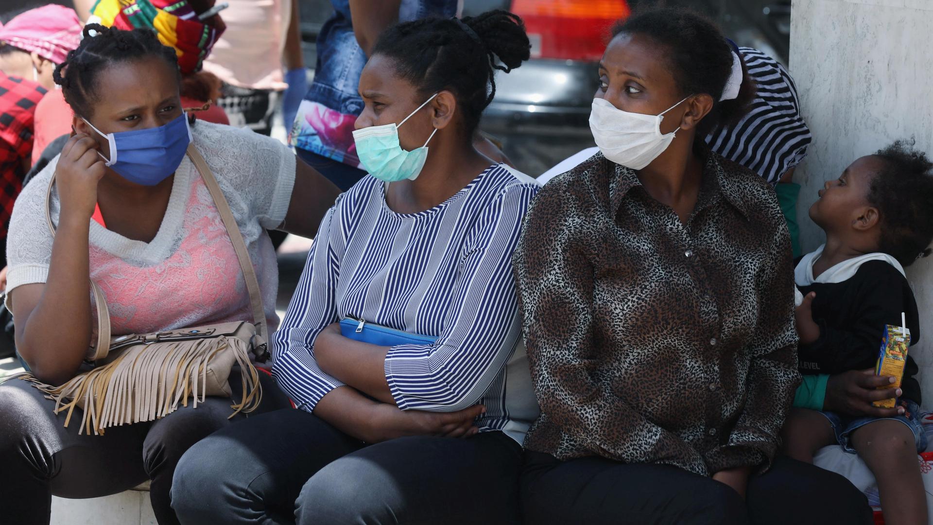 Four Ethiopian women wearing blue face masks sit outside with a young child. 