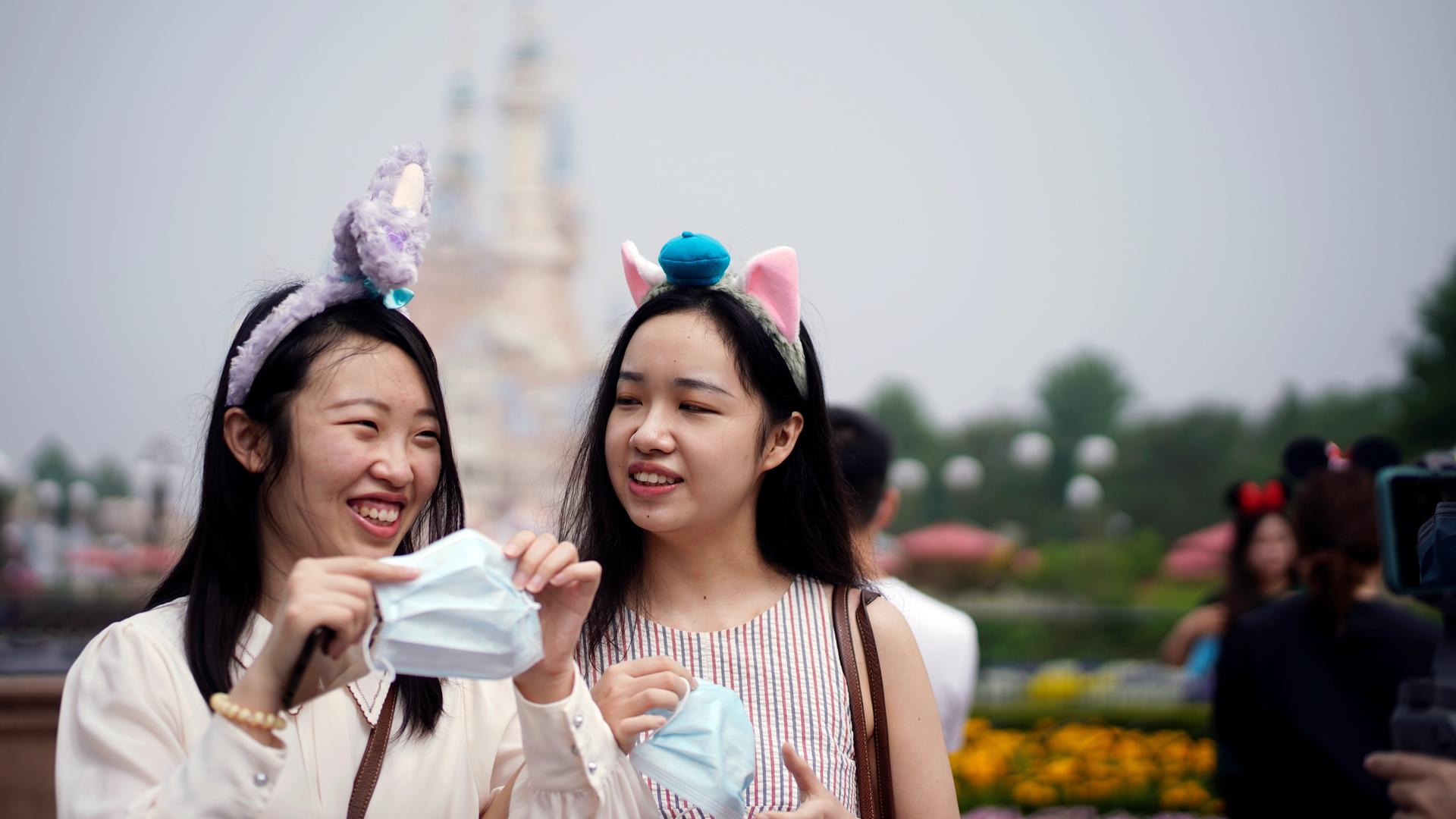 Two young women with headbands hold face masks at the Shanghai Disneyland theme park as it reopens following a shutdown due to the coronavirus disease