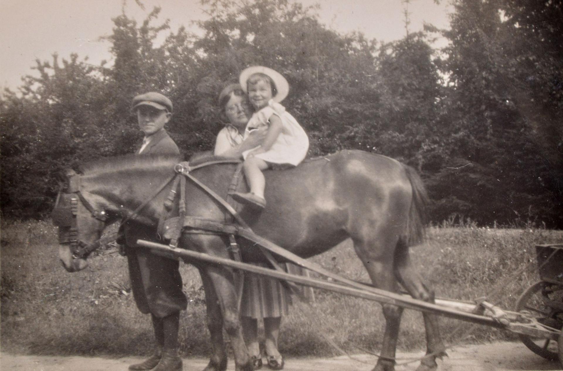 A black and white photograph of girl on a pony with two people around her