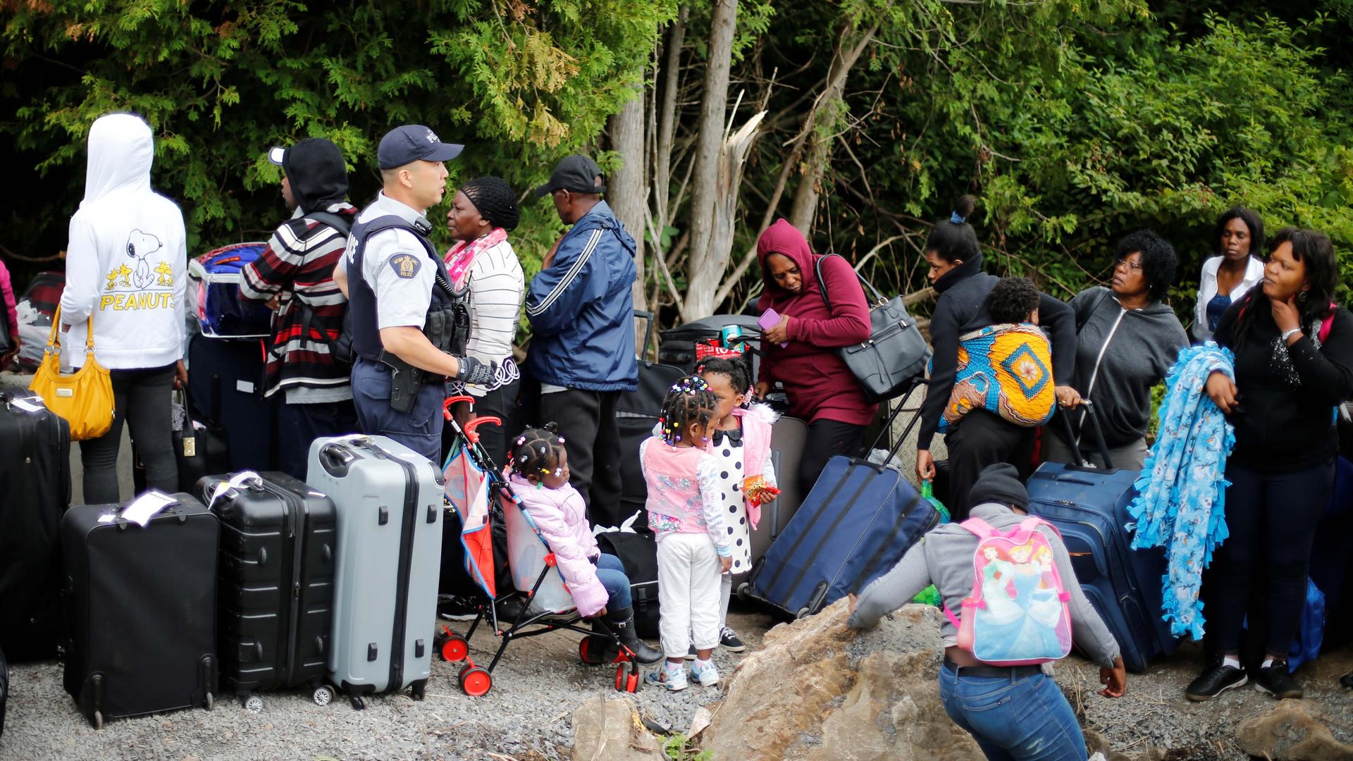 A Royal Canadian Mounted Police (RCMP) officer announces to a group of asylum-seekers that they will be crossing illegally into Canada as they wait in line to to enter at the US-Canada border in Champlain, New York, August 7, 2017.