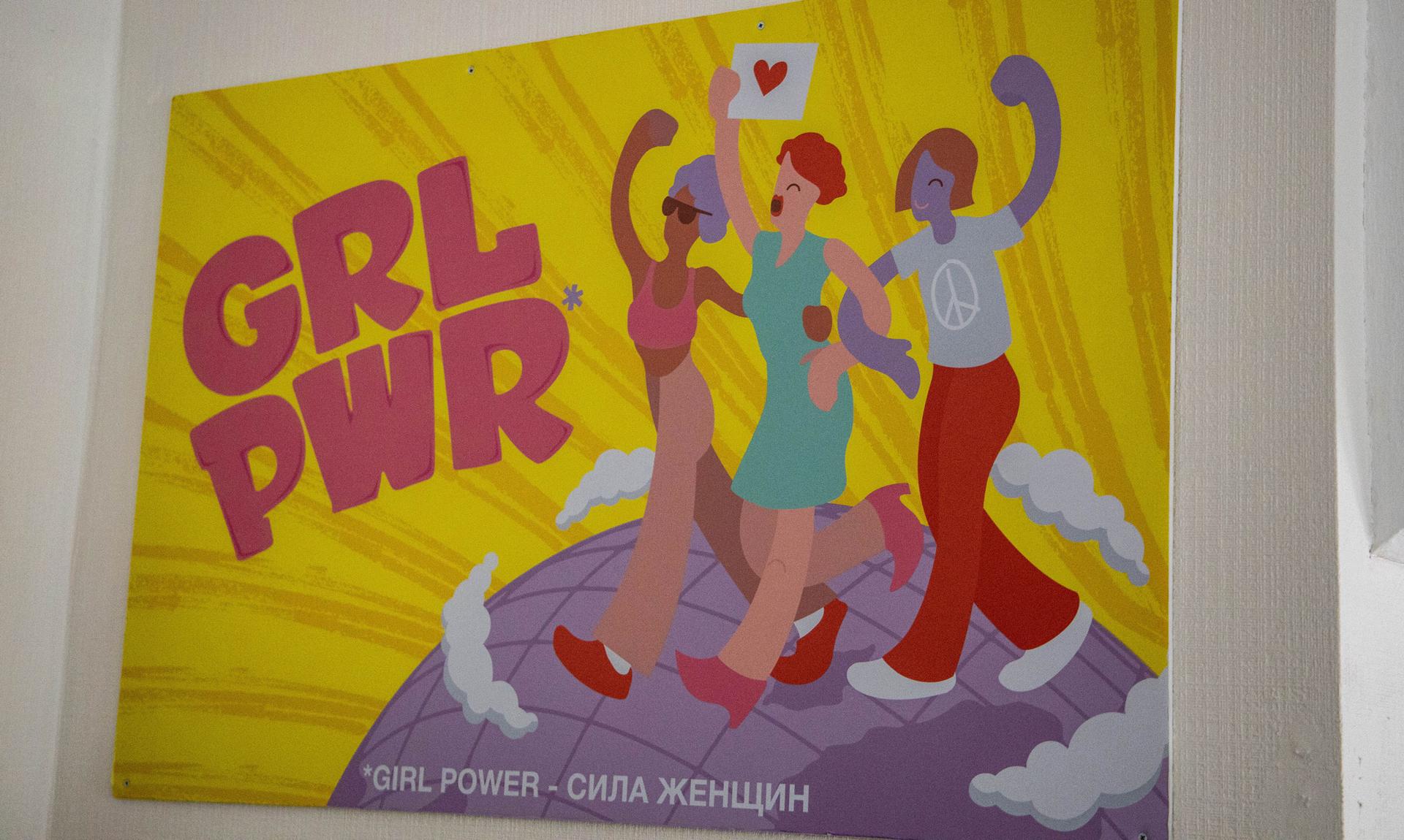 An illustrated poster shows three women linked arm in arm walking on a globe and it says GRL PWR.