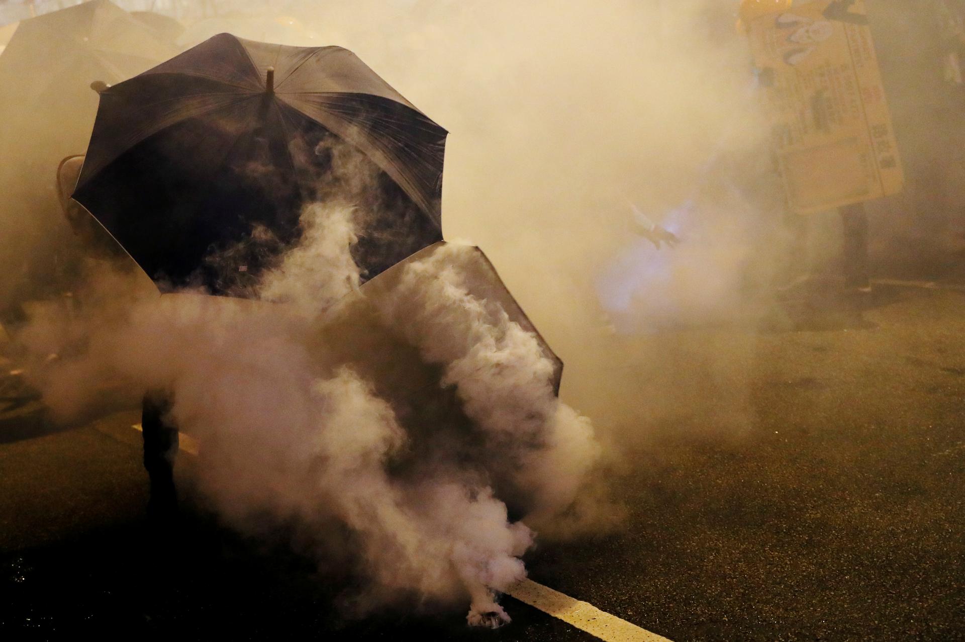 Protesters hold umbrellas in thick tear gas. 