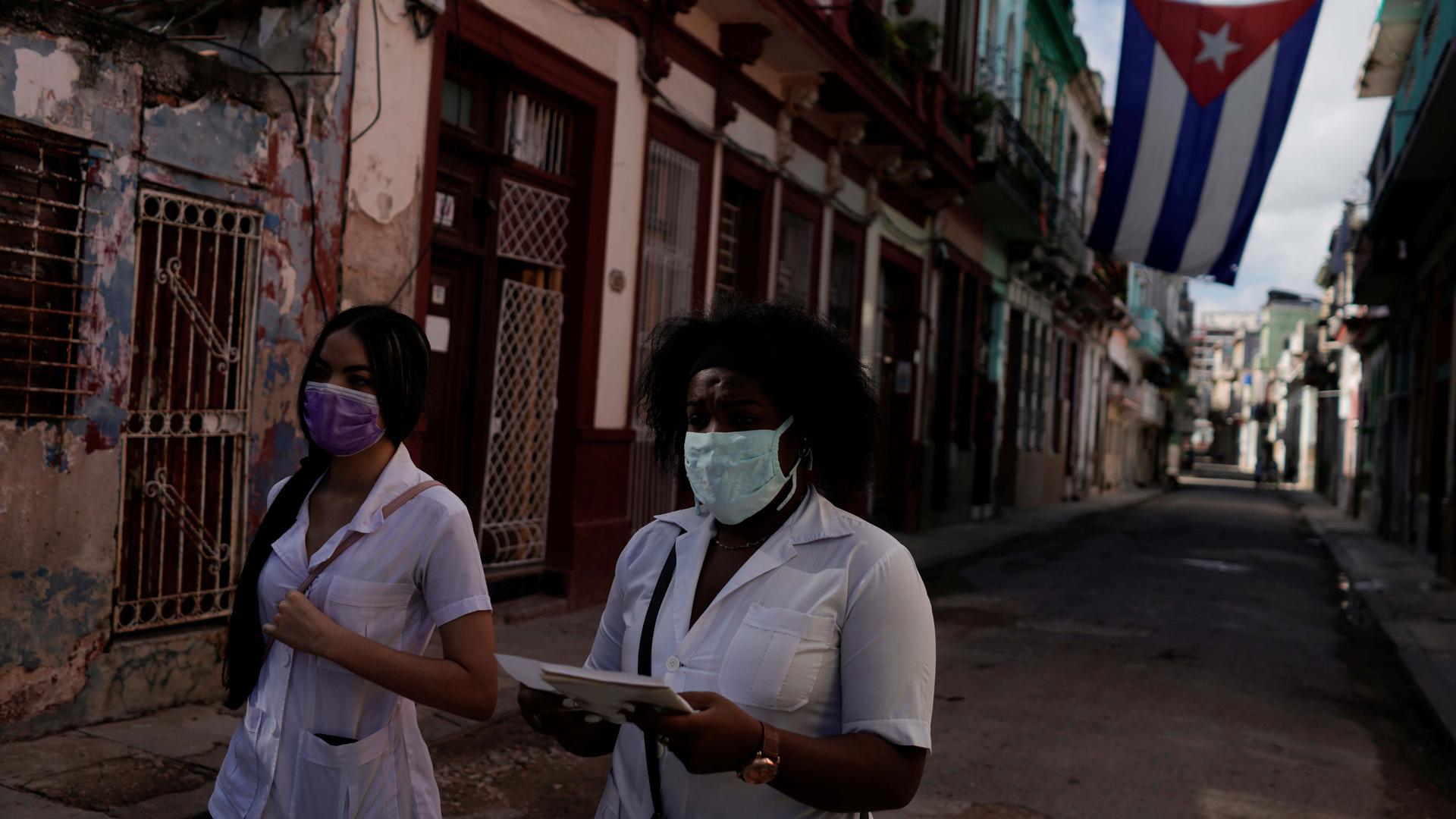 Medical students walk past a Cuban flag as they check door to door for people with symptoms amid concerns about the spread of the coronavirus disease (COVID-19), in downtown Havana, Cuba, May 12, 2020.