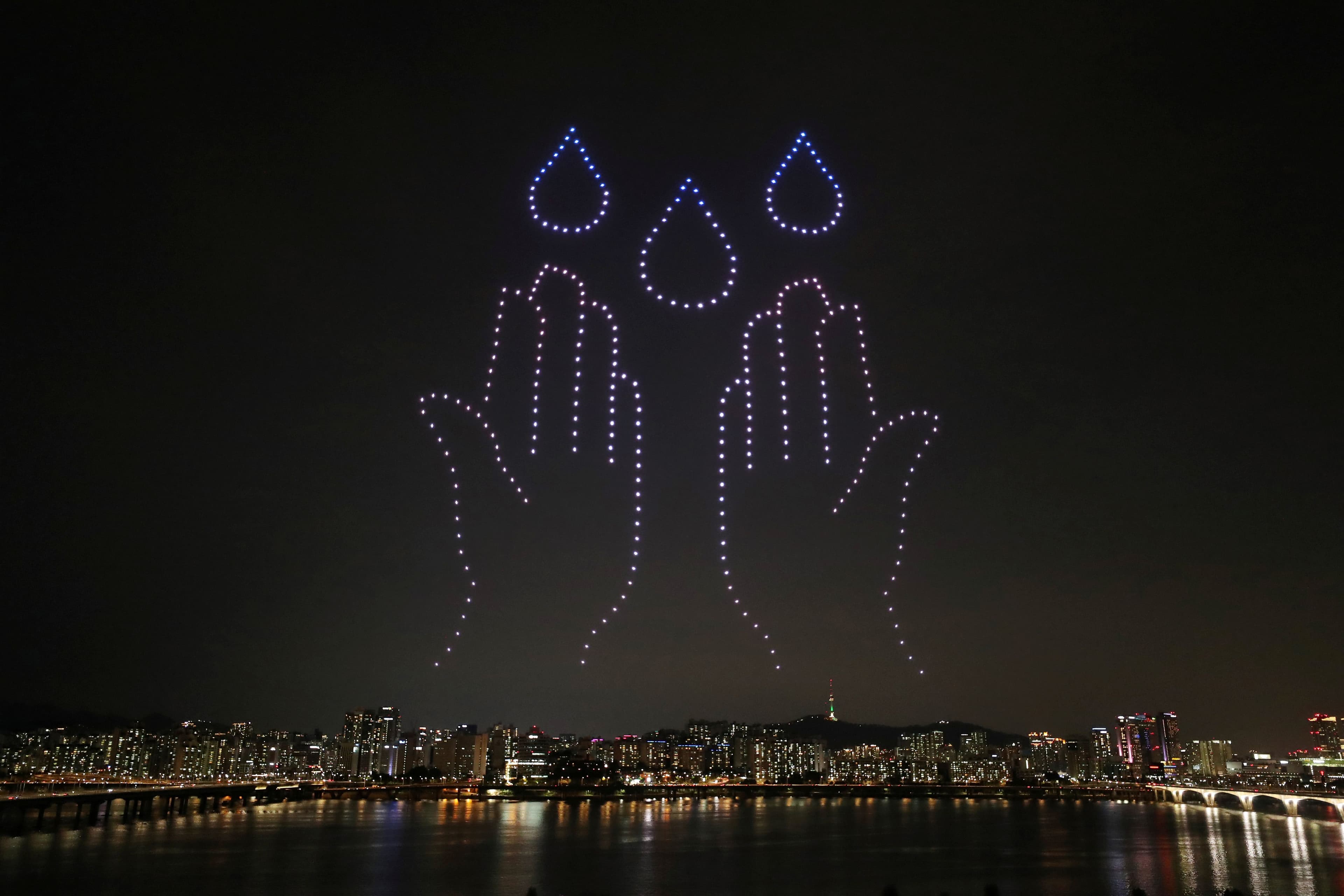 Two hand and three drops of water are drawn in the sky with the lights of small drones in Seoul.
