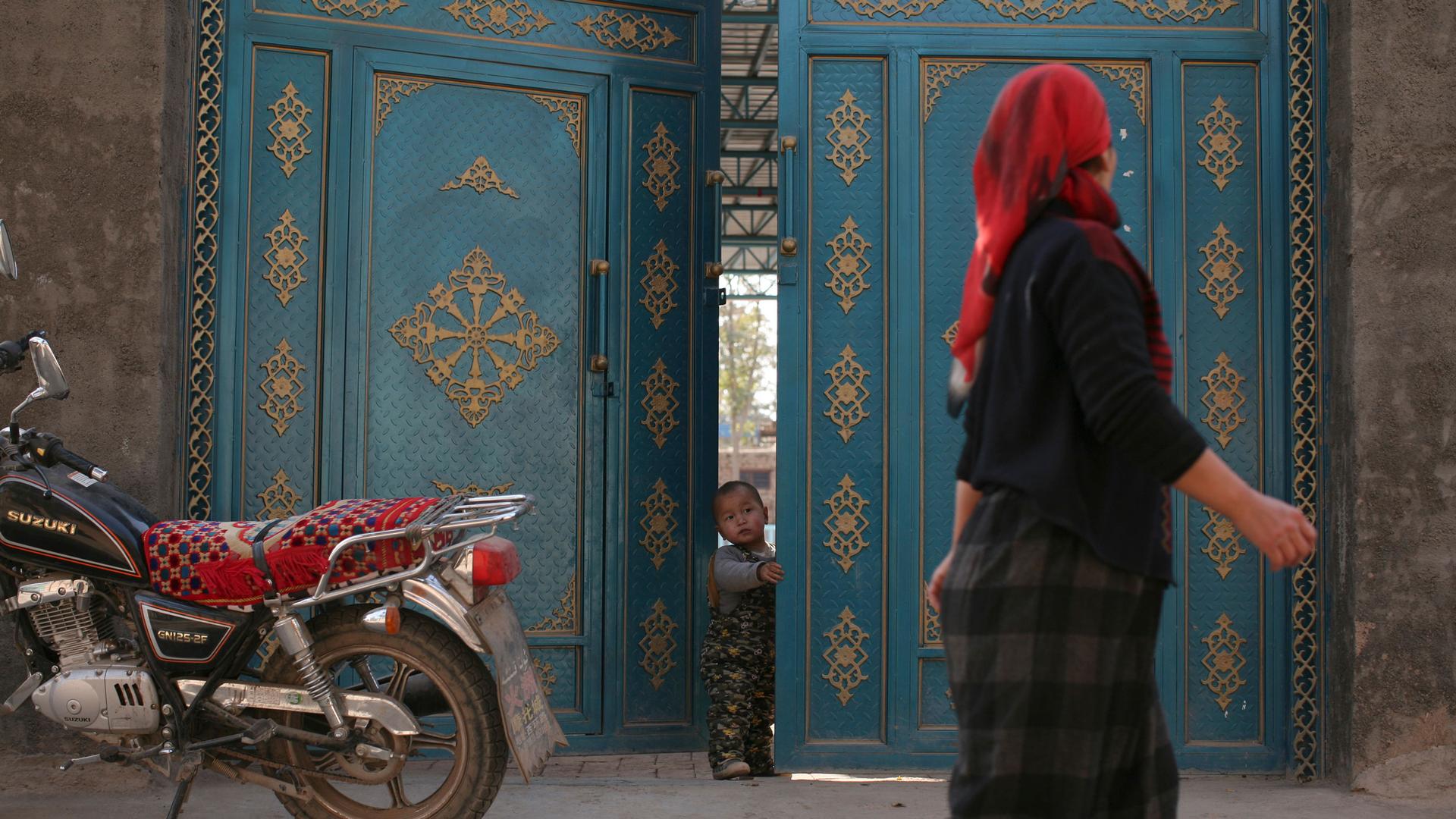 A child looks out from a door as a Uighur woman walks by