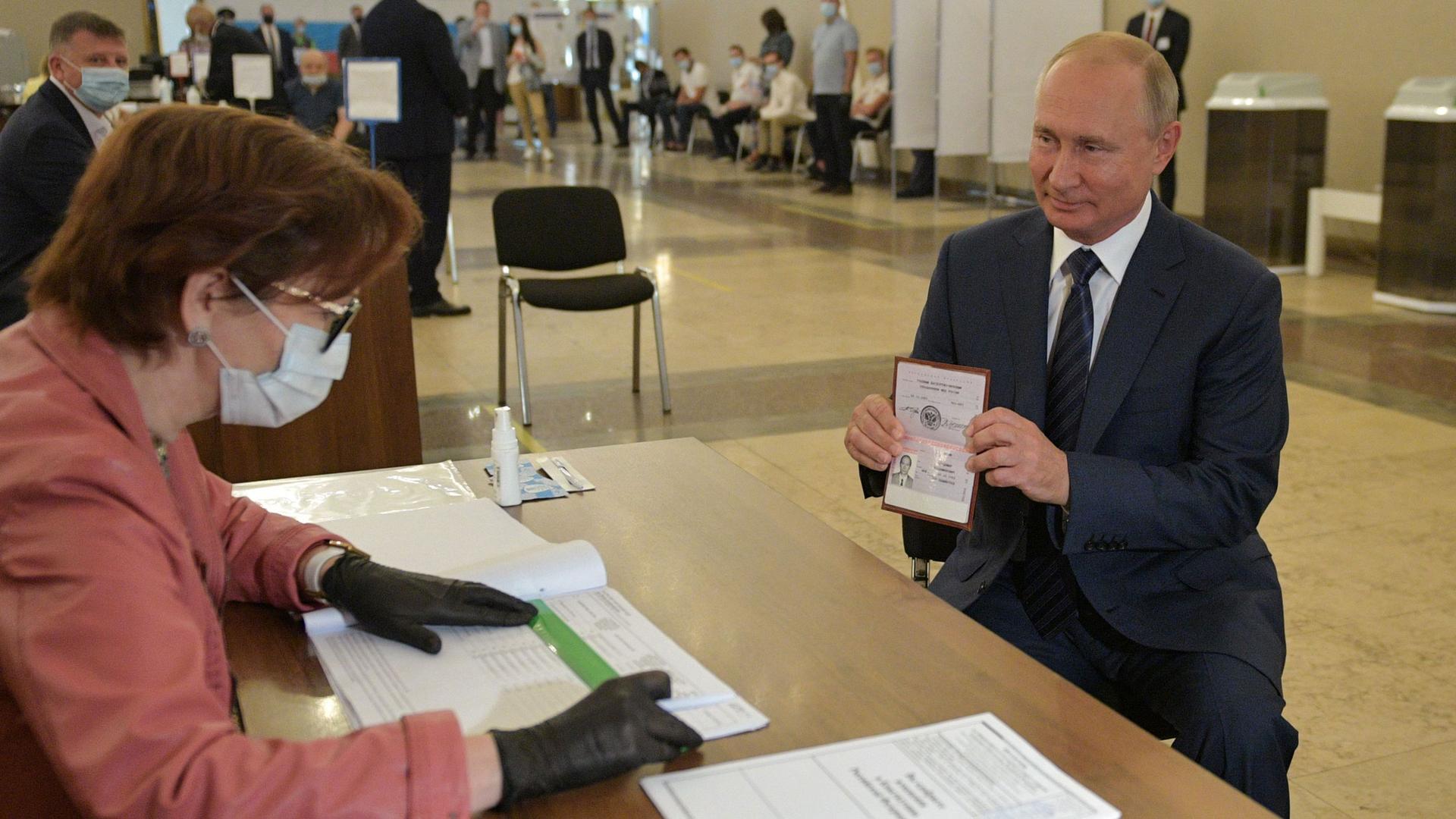 Putin holds his passport in front of an election official 