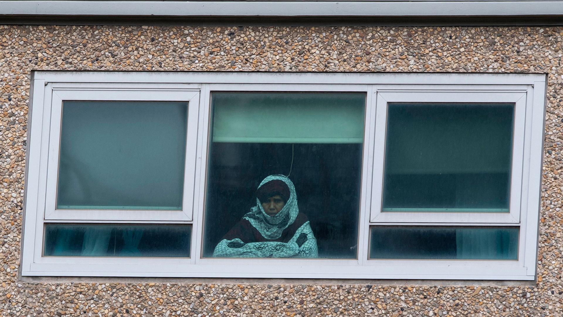 A woman is shown from looking through a window and wearing a shirt with a hood over her head.