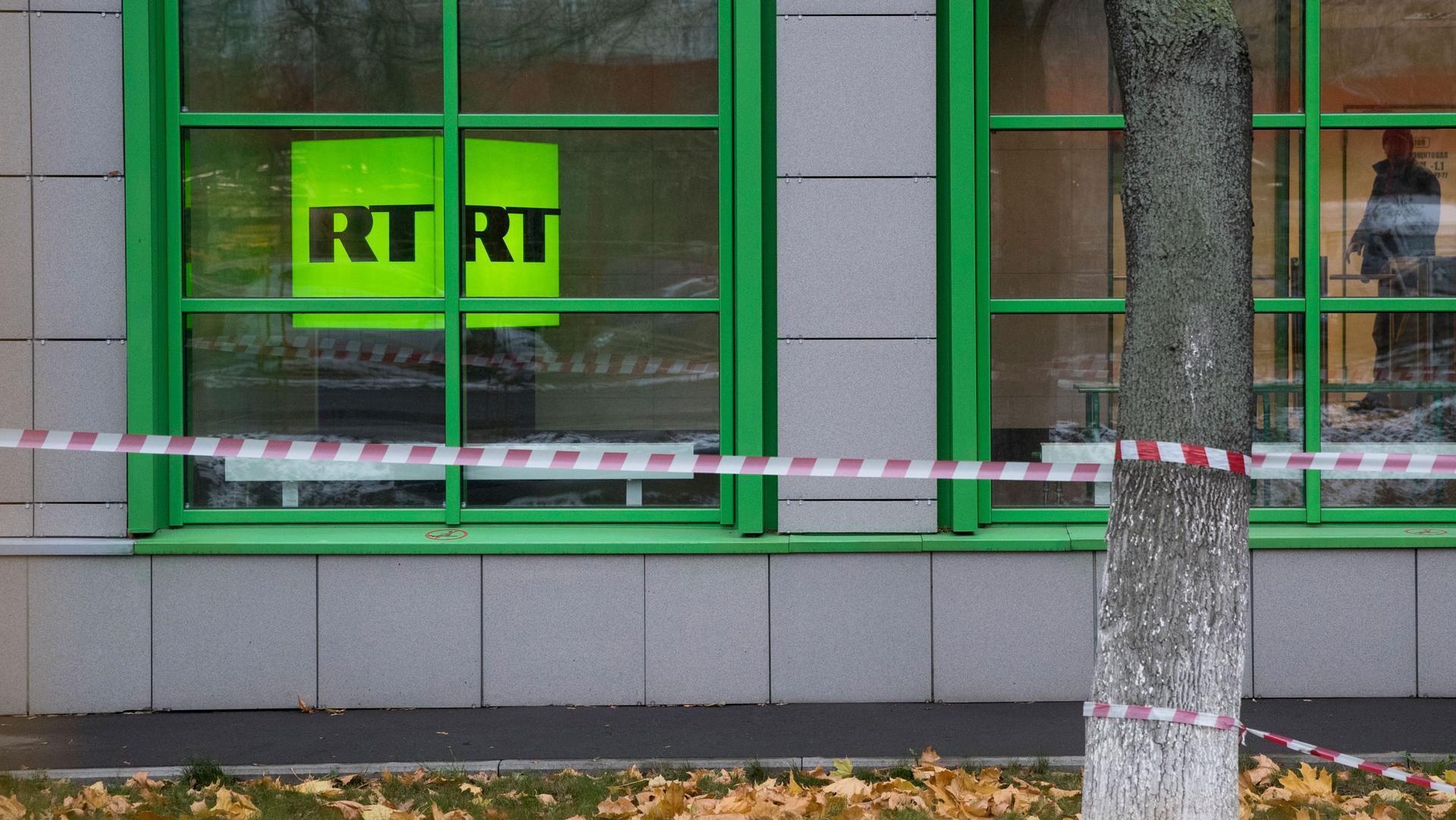 Russian state-owned television station RT logo is seen through a window with caution tape in front of a building