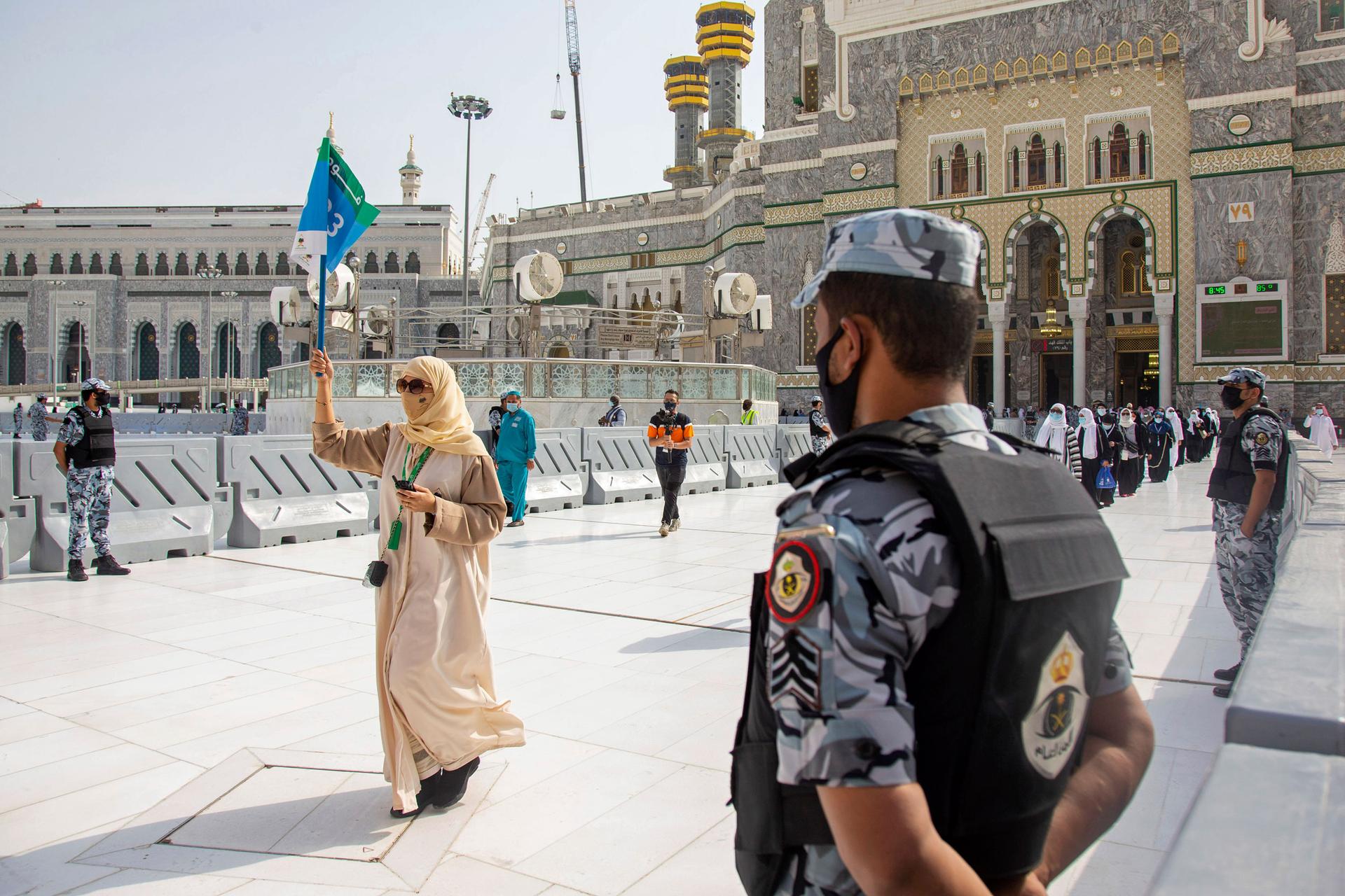 A security official is shown in the near ground with a woman in the distance walking and holding up a guide flag.